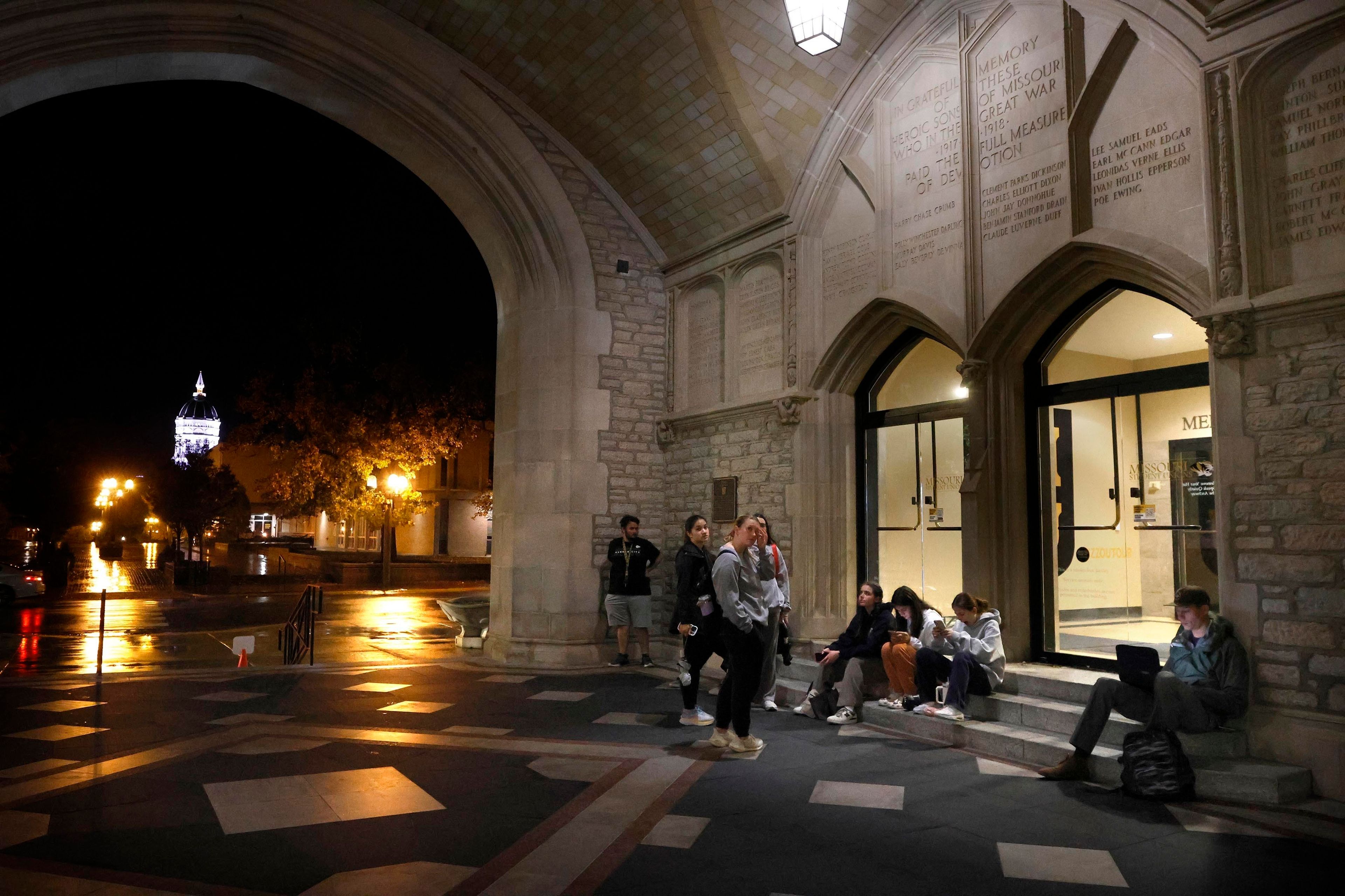 Jessie Hall glows in the background as people wait for polls to open under the arch at Memorial Union on the University of Missouri campus in Columbia, Mo. on Tuesday, Nov. 5, 2024. Polls opened at 6 a.m. and a line formed early. (Hannah Henderson/Missourian via AP)