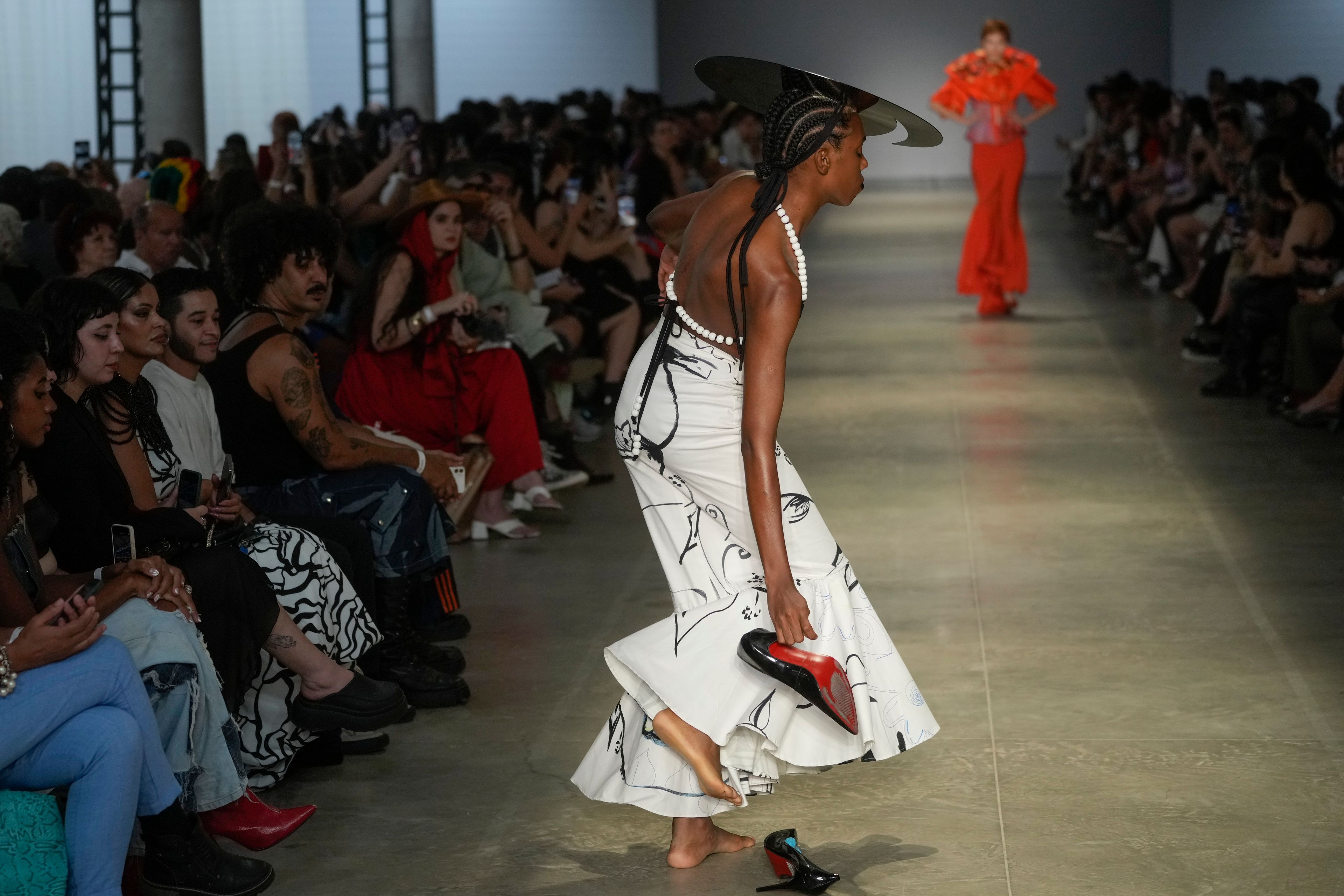 A model takes off her shoes while on the catwalk during the presentation of the Cria Costura collection at Sao Paulo Fashion Week in Sao Paulo, Thursday, Oct. 17, 2024. (AP Photo/Andre Penner)