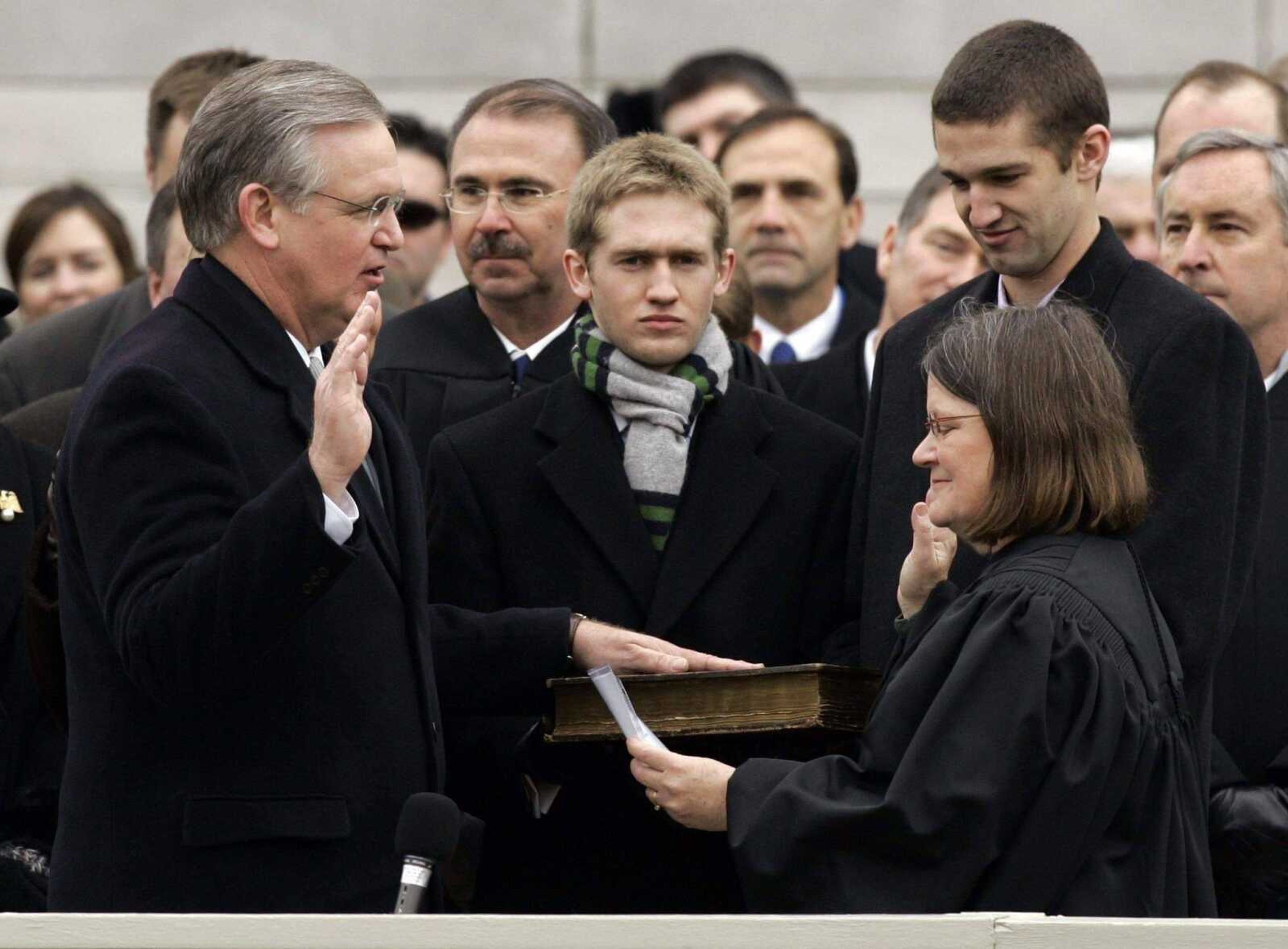 JEFF ROBERSON ~ Associated Press<br>Missouri governor-elect Jay Nixon, left, is sworn in Monday as the state's 55th governor by Missouri Supreme Court Chief Justice Laura Denvir Stith, right, as Nixon's sons Jeremiah, center, and Will, back right, look on in Jefferson City, Mo.