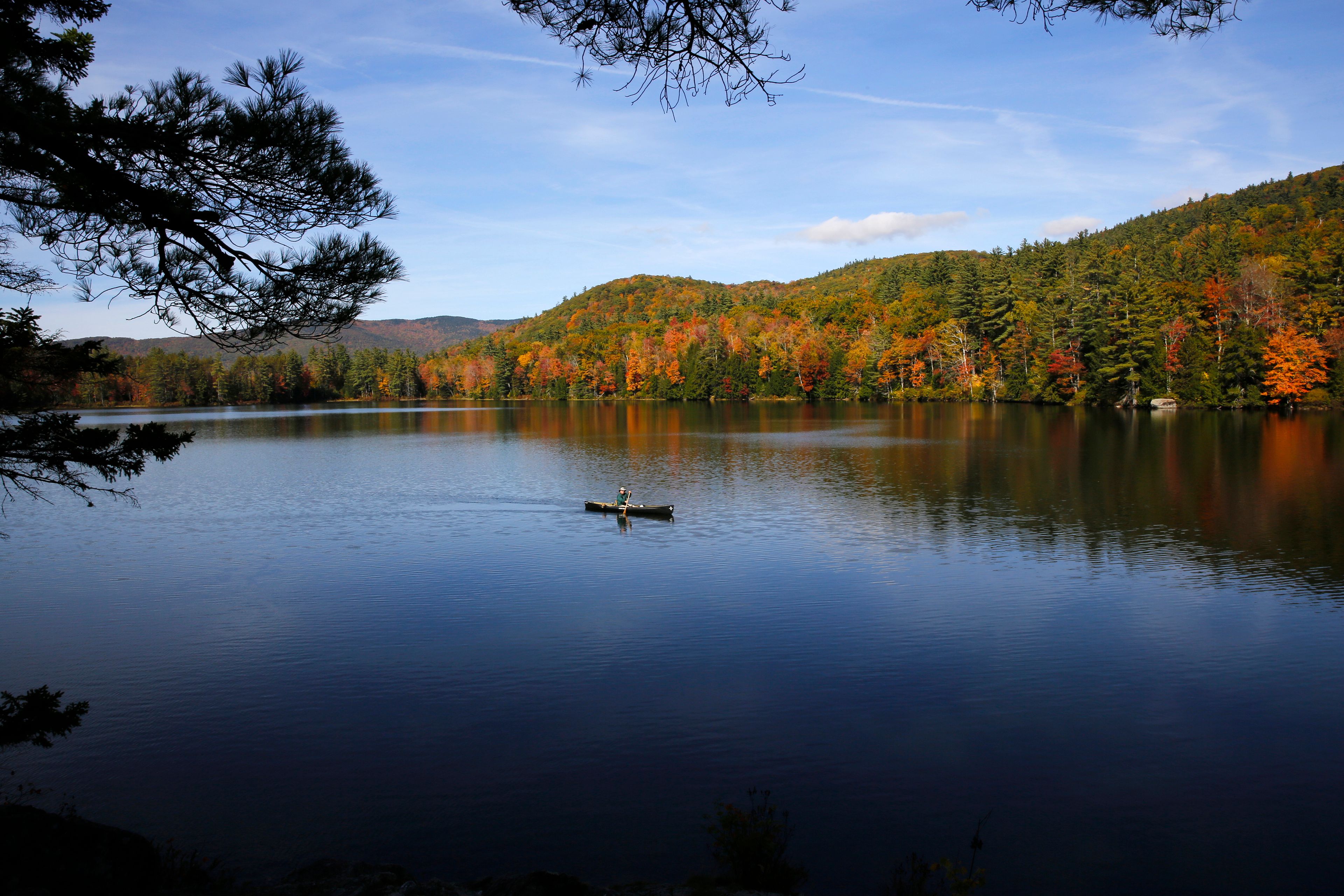 A fly fisherman paddles on a pond as fall foliage begins to show color in Campton, N.H., Sunday, Oct. 6, 2024. (AP Photo/Caleb Jones)