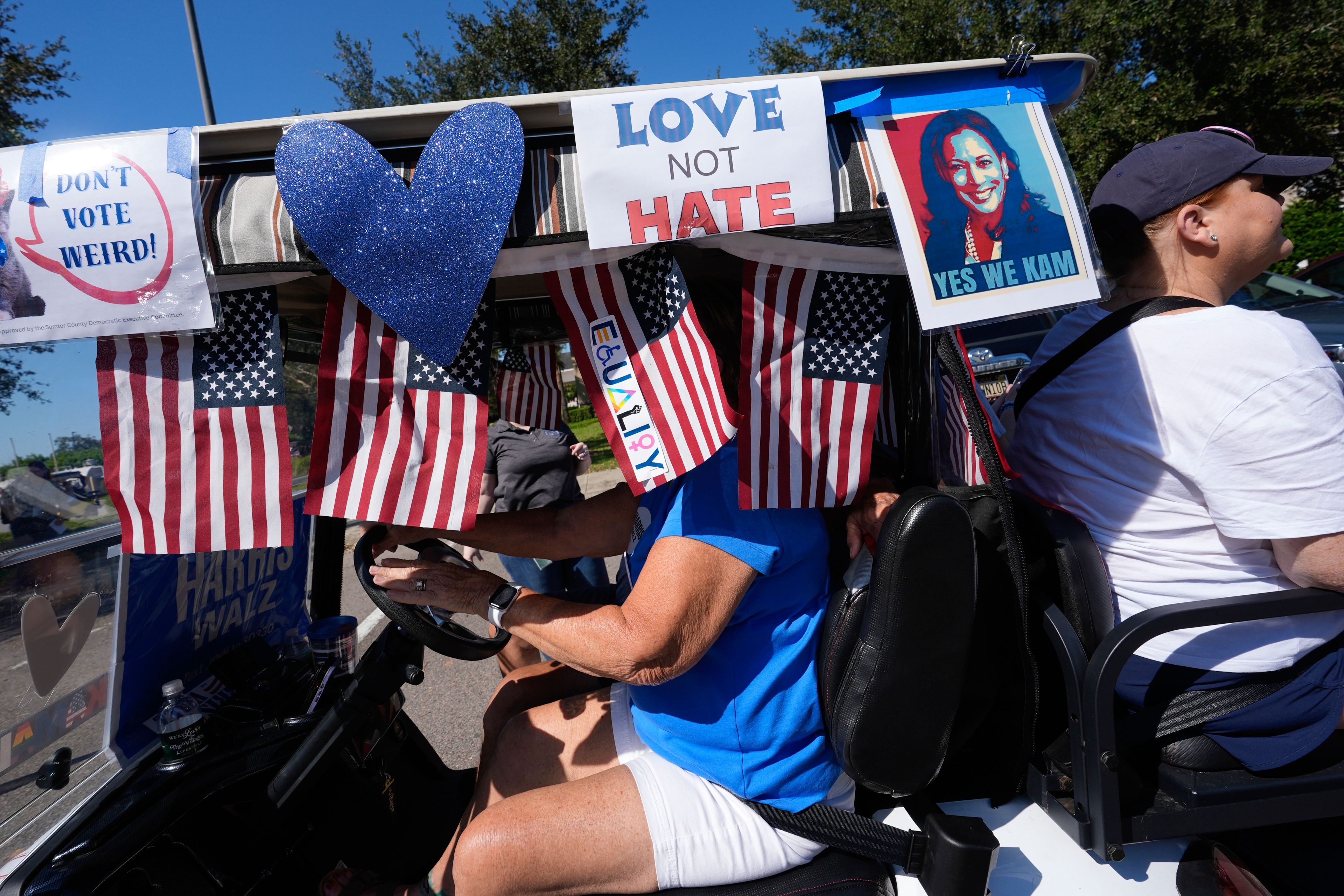 Voters ride in a decorated cart as hundreds of supporters of Democratic presidential nominee Vice President Kamala Harris parade in golf carts to deliver mail-in votes organized by the Villages Democratic Club, in The Villages, Fla., Monday, Oct. 14, 2024. (AP Photo/Rebecca Blackwell)