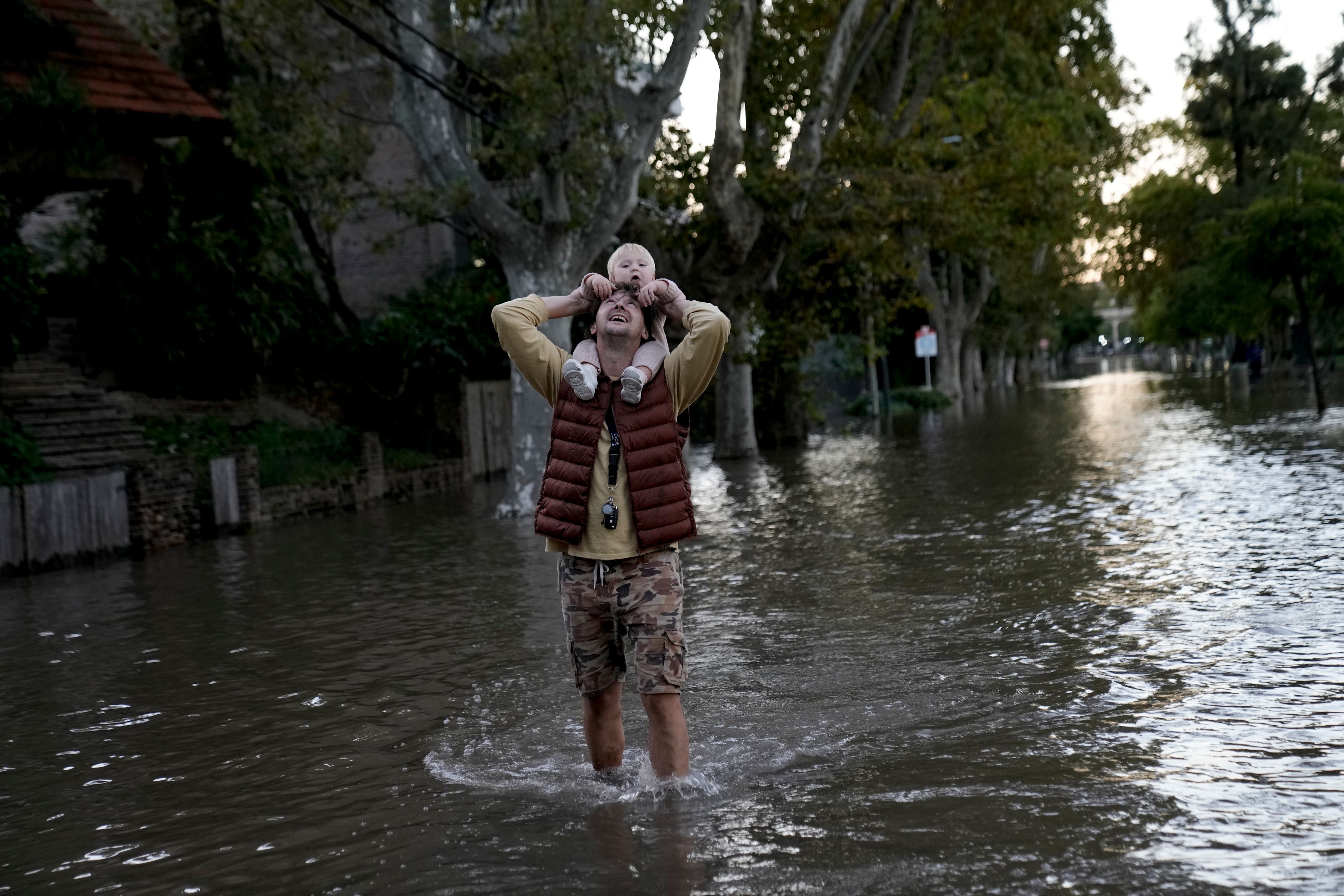 FILE - Alex Pusharev holds his daughter Miroslava while wading through a street flooded due to the rise of the water levels of the Rio de la Plata River, in Tigre, on the outskirts of Buenos Aires, Argentina, March 21, 2024. (AP Photo/Rodrigo Abd, File)