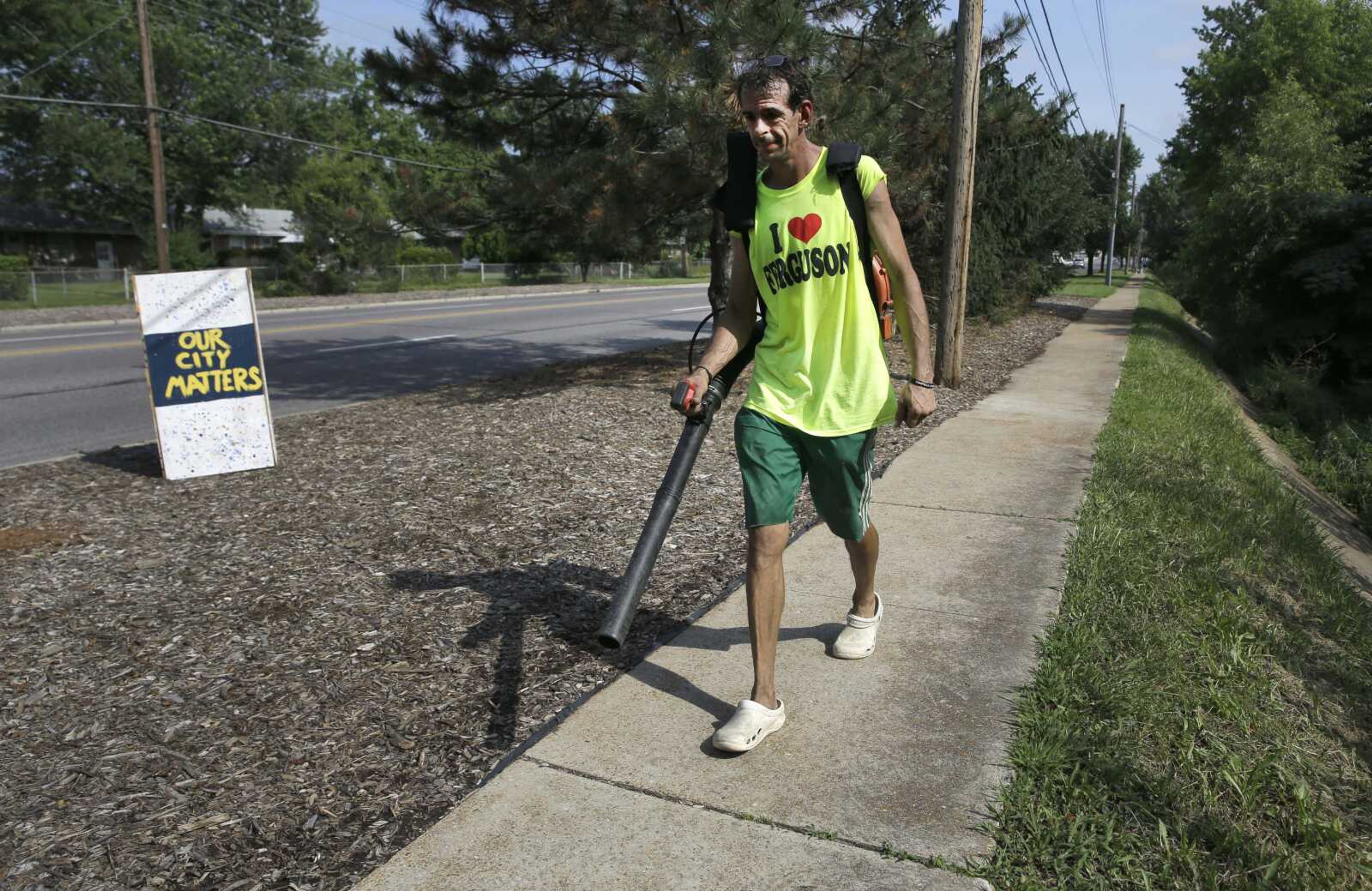 Mike Brandon uses a blower to clean a sidewalk Monday along West Florissant Avenue Monday in Ferguson, Missouri. Hundreds of volunteers converged on the area for a litter-pickup and weeding effort led by a local radio station before the Aug. 9 one-year anniversary of Michael Brown's death. (Jeff Roberson ~ Associated Press)