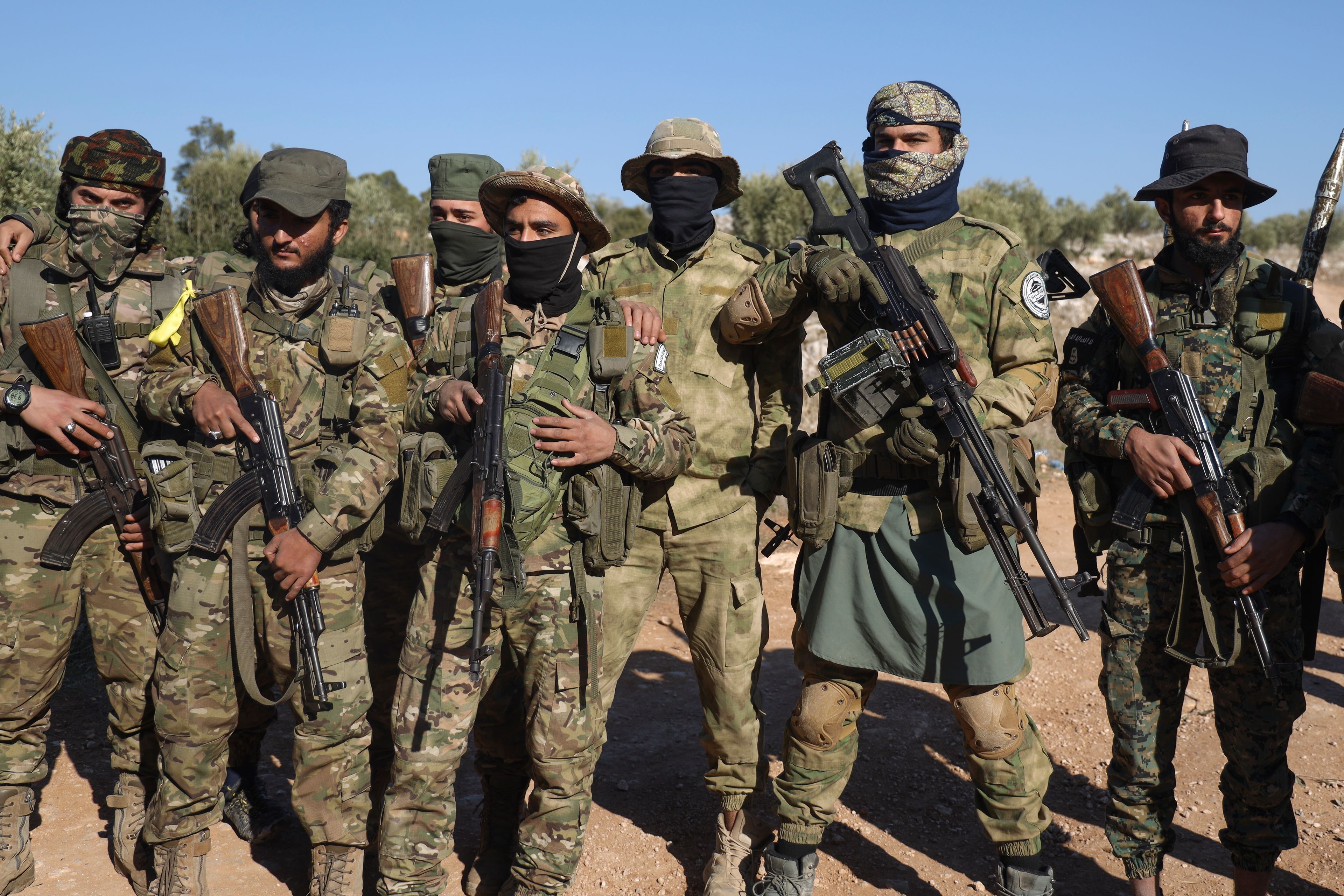 Syrian opposition fighters stand in formation after entering the village of Anjara, western outskirts of Aleppo, Syria, Thursday Nov. 28, 2024, part of their major offensive on government-controlled areas in the country's northwestern Syria. (AP Photo/Omar Albam)