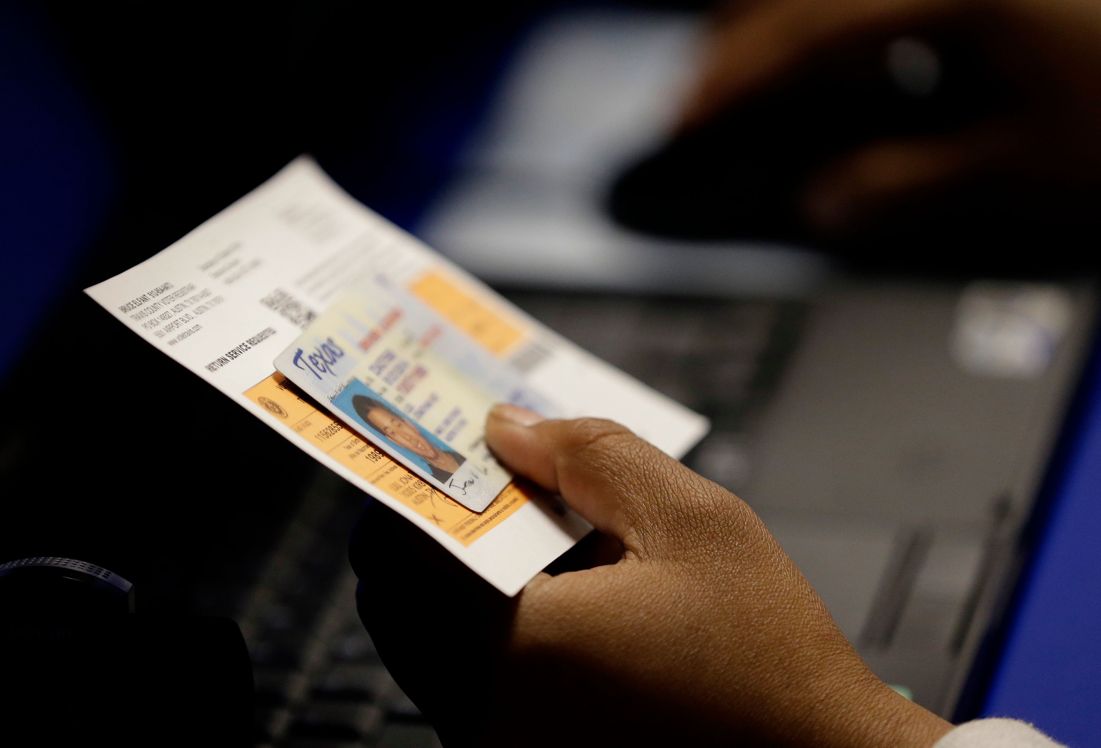 FILE - An election official checks a voter's photo identification at an early voting polling site in Austin, Texas, Feb. 26, 2014. (AP Photo/Eric Gay, File)