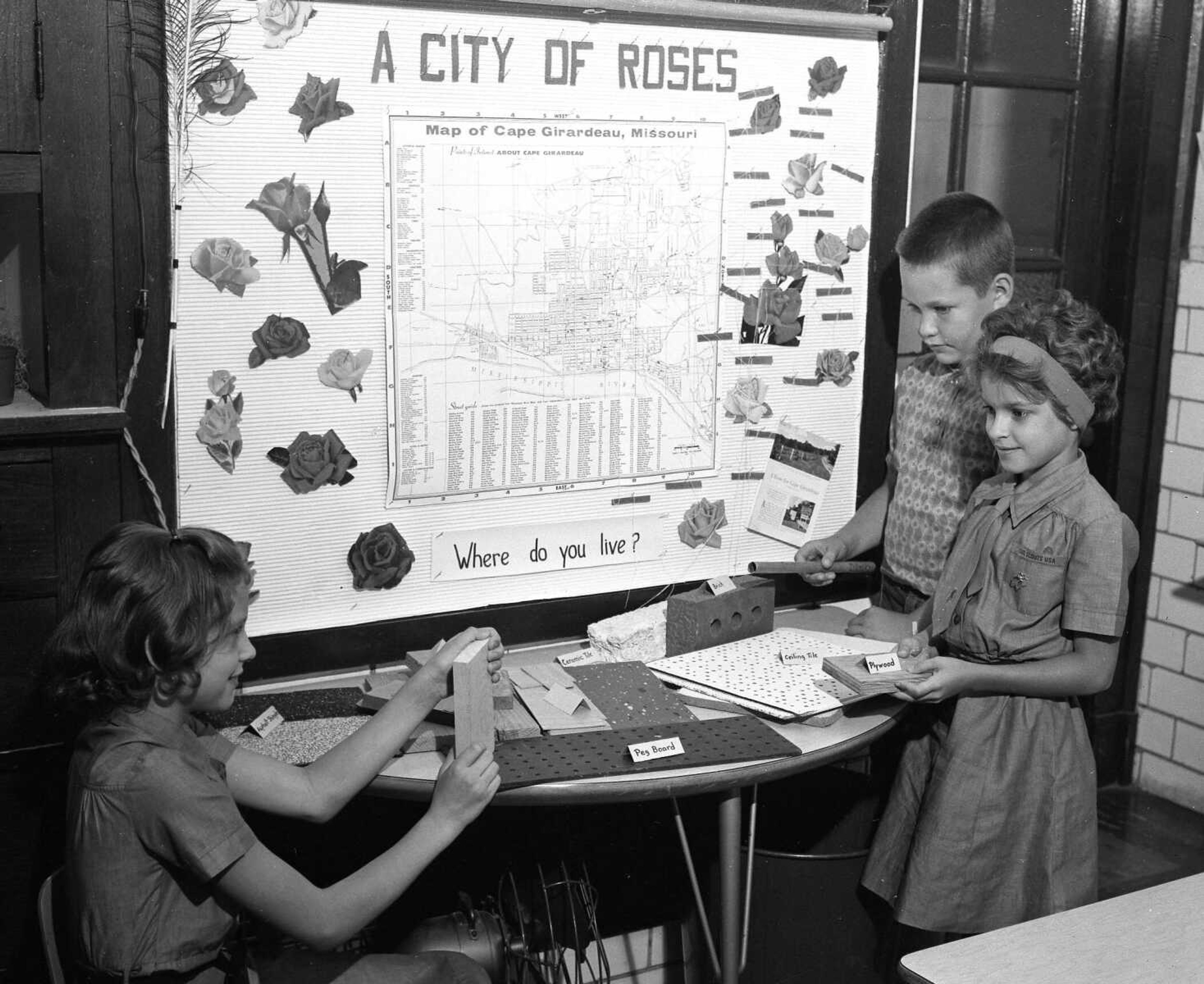 Oct. 12, 1963 Southeast Missourian.
Ann Vogel, seated, Greg Hoxworth and Donna Barklage brought numerous items for a building materials display their third grade class participated in at Campus School. Each item was labeled for the special study on homes. (G.D. Fronabarger/Southeast Missourian archive)

Children in Mrs. Raymond Sheets’ third grade class at Campus School brought their homes into the classroom for a recent social studies unit on “Homes.” Pupils prepared a “City of Roses” bulletin board showing a map of Cape Girardeau, accompanied with the query, “Where do you live?”

The building materials display was loaded with items brought by the youngsters, such as lumber, brick, stone, tile, marble, slate, glass, iron pipes, hardware and asphalt shingles.