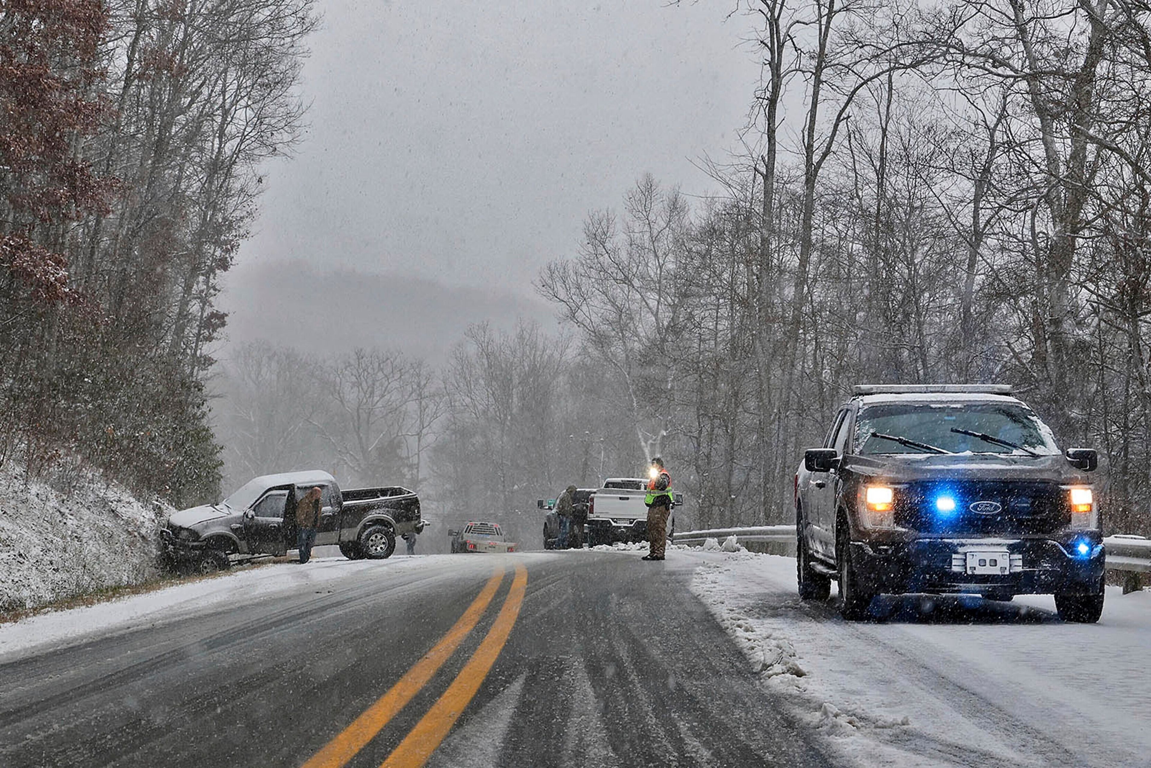 A driver, left, waits for his truck to be removed from an accident site after sliding into a hillside during snow showers, Thursday, Nov. 21, 2024, near Quinwood, W.Va. (Jenny Harnish/The Register-Herald via AP)