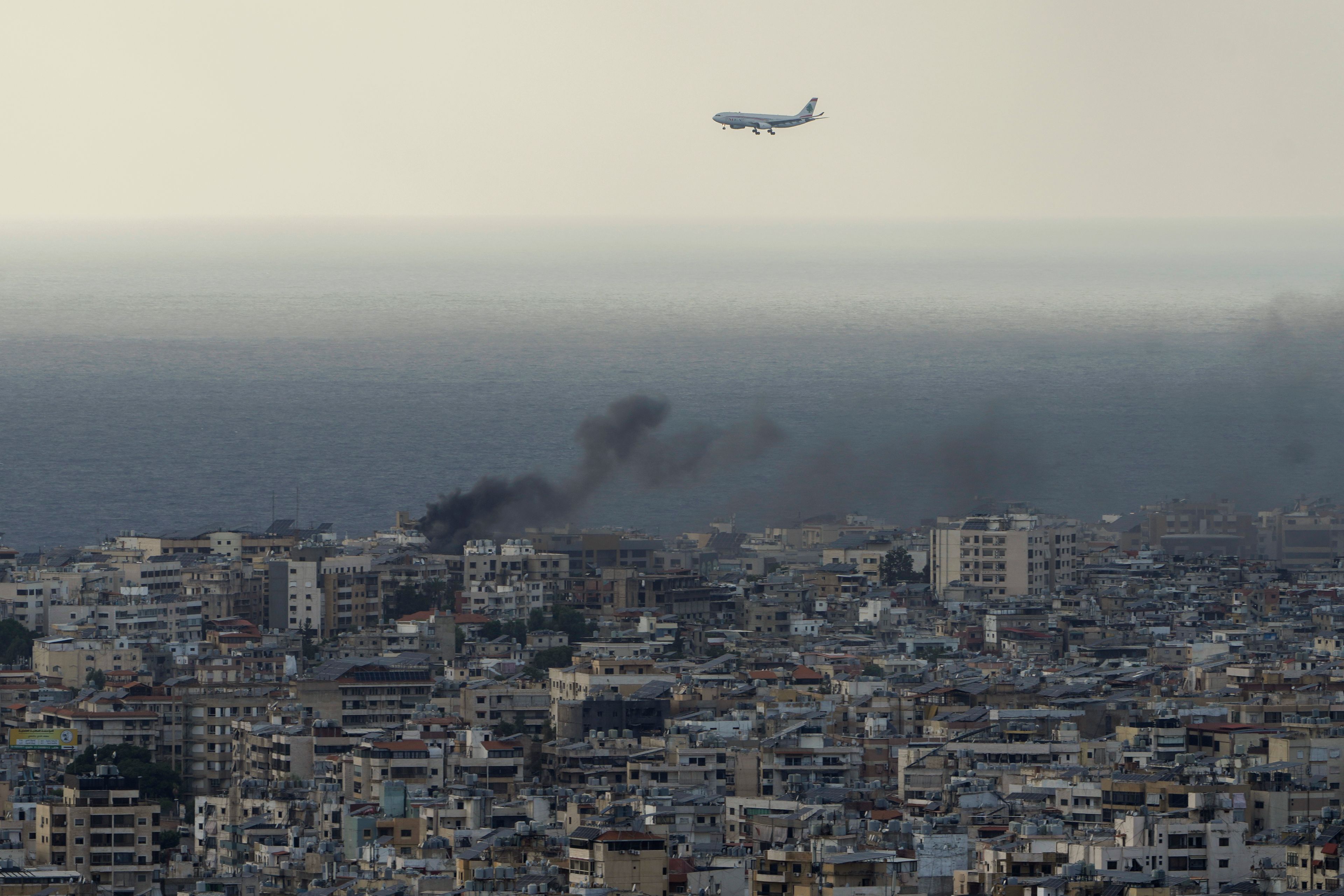 A Middle East Airlines airplane flies over Beirut as smoke rises from Israeli airstrikes in Dahiyeh, Beirut, Tuesday, Oct. 1, 2024. (AP Photo/Bilal Hussein)