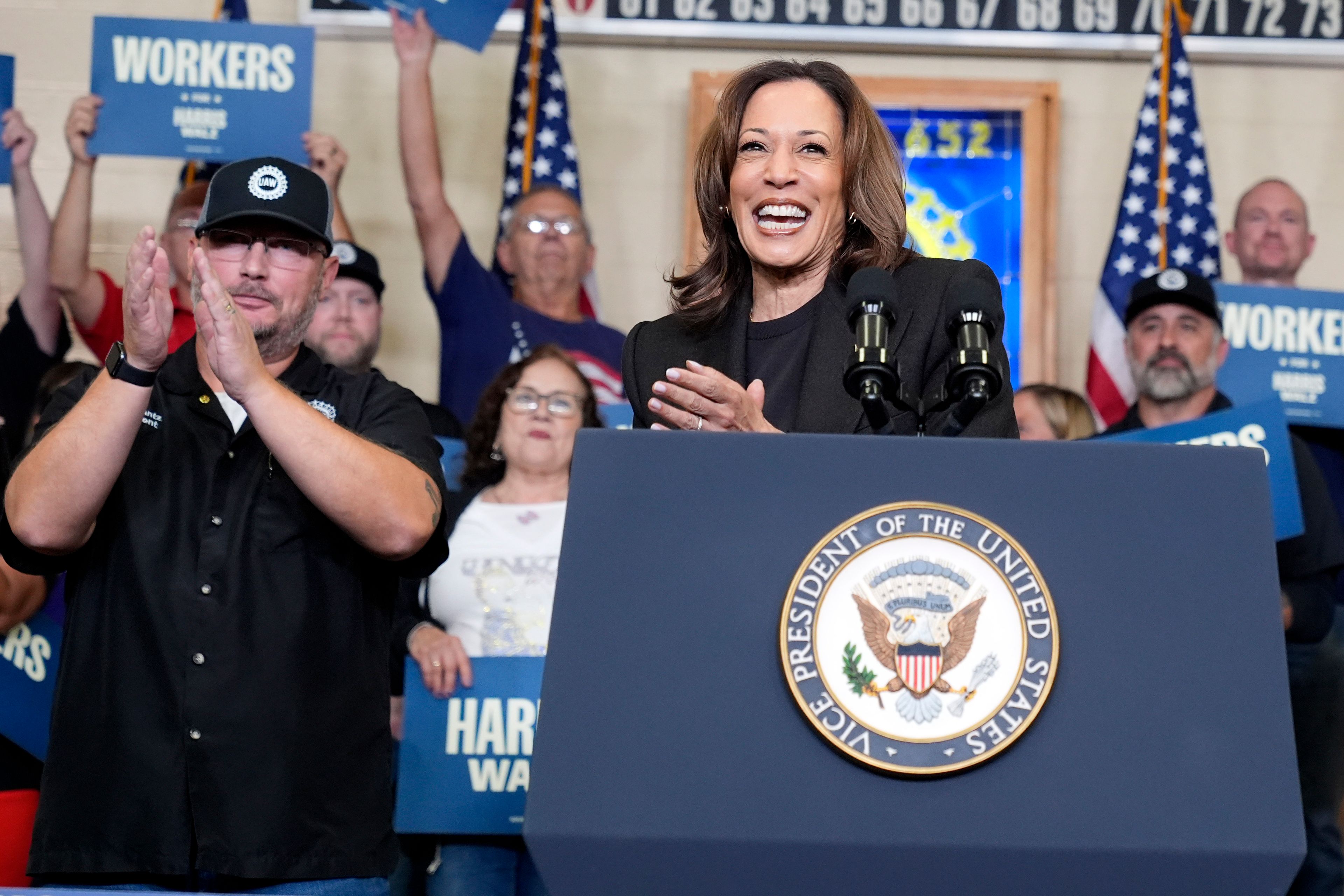 Democratic presidential nominee Vice President Kamala Harris speaks as Benjamin Frantz, left, president of UAW Local 652, looks on at UAW Local 652 during a campaign event in Lansing, Mich., Friday, Oct. 18, 2024. (AP Photo/Jacquelyn Martin)