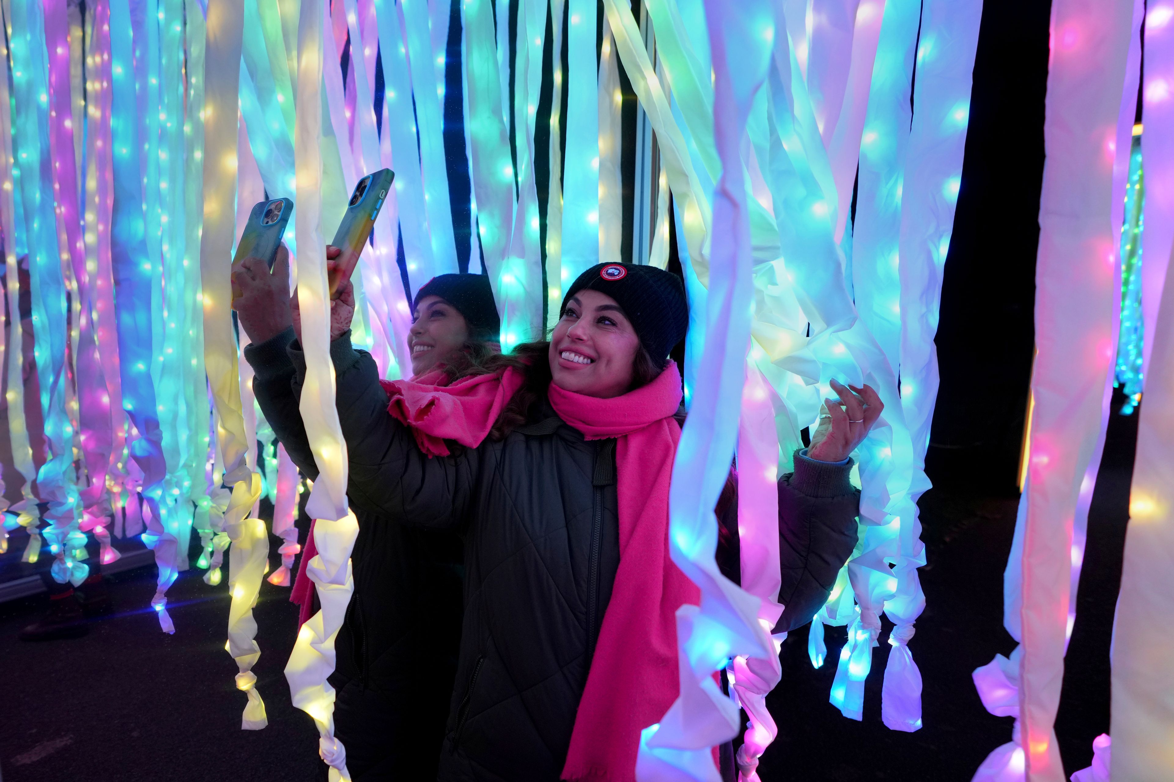 A woman takes a picture at the 'Christmas Presents' on the Christmas light trail as it returns for its 12th year with a showcase of new installations set within the UNESCO World Heritage Site landscape of Kew Gardens in London, England, Tuesday, Nov. 12, 2024. (AP Photo/Kirsty Wigglesworth)