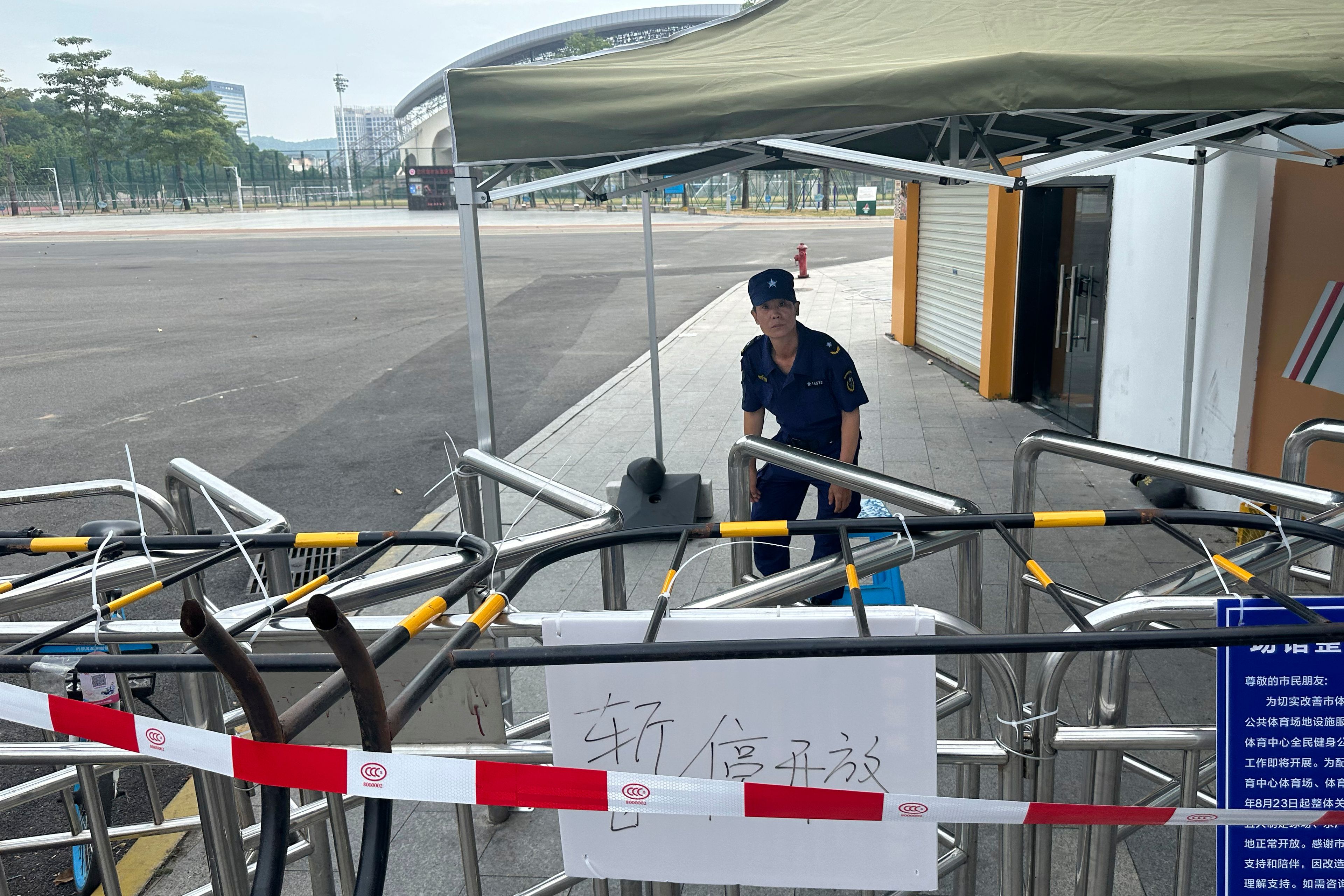 A security guard looks at inside the barricaded entrance to the "Zhuhai People's Fitness Plaza" where a man rammed his car into people exercising at the sports center, in Zhuhai in southern China's Guangdong province on Wednesday, Nov. 13, 2024. Sign in white reads "Temporarily Closed". (AP Photo/Ng Han Guan)