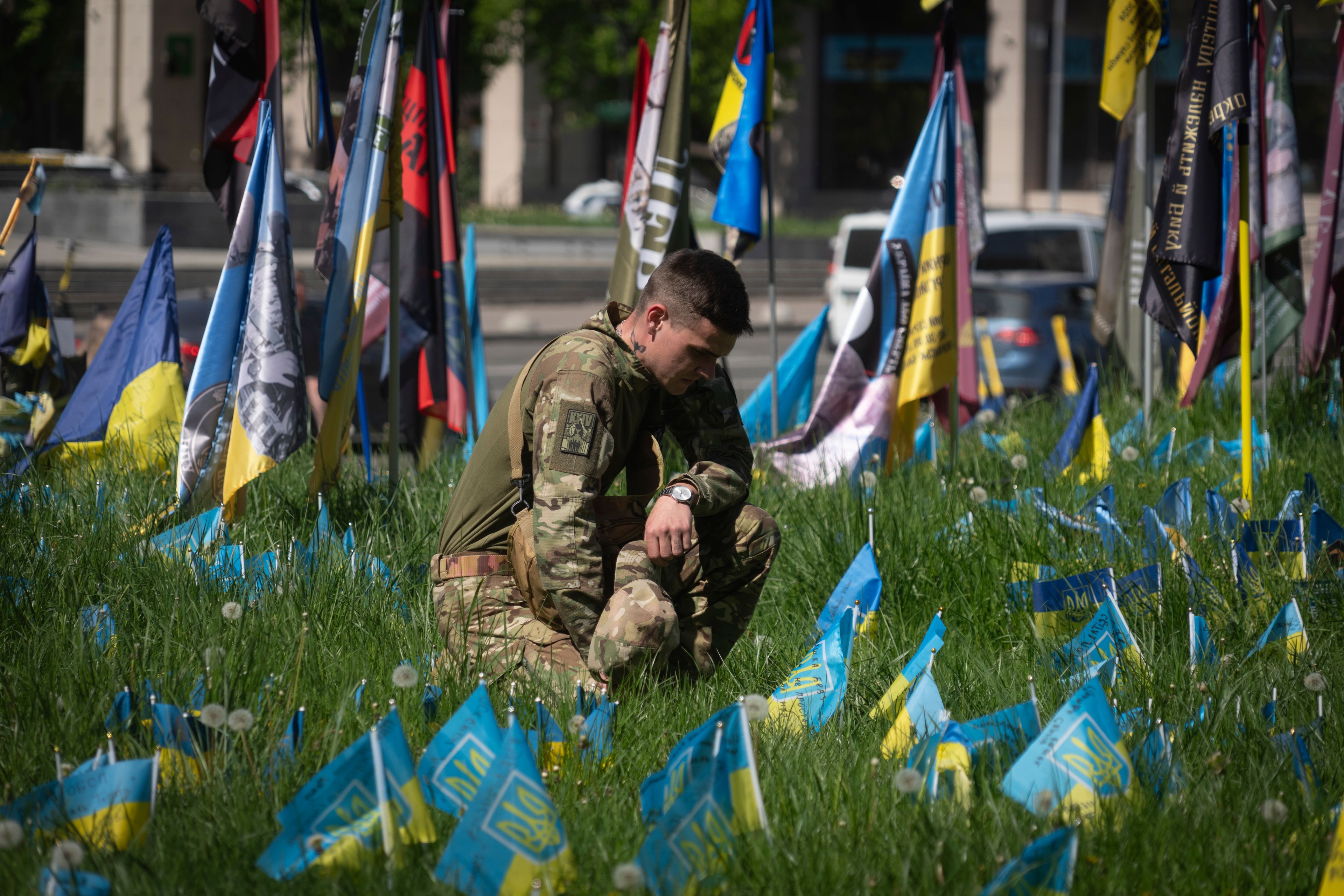 A Ukrainian soldier installs a small national flag on a grassed area at the Independence Square in Kyiv, Ukraine, Wednesday, May 1, 2024, to commemorate his fellow soldier killed in a battle with the Russian troops . (AP Photo/Efrem Lukatsky)