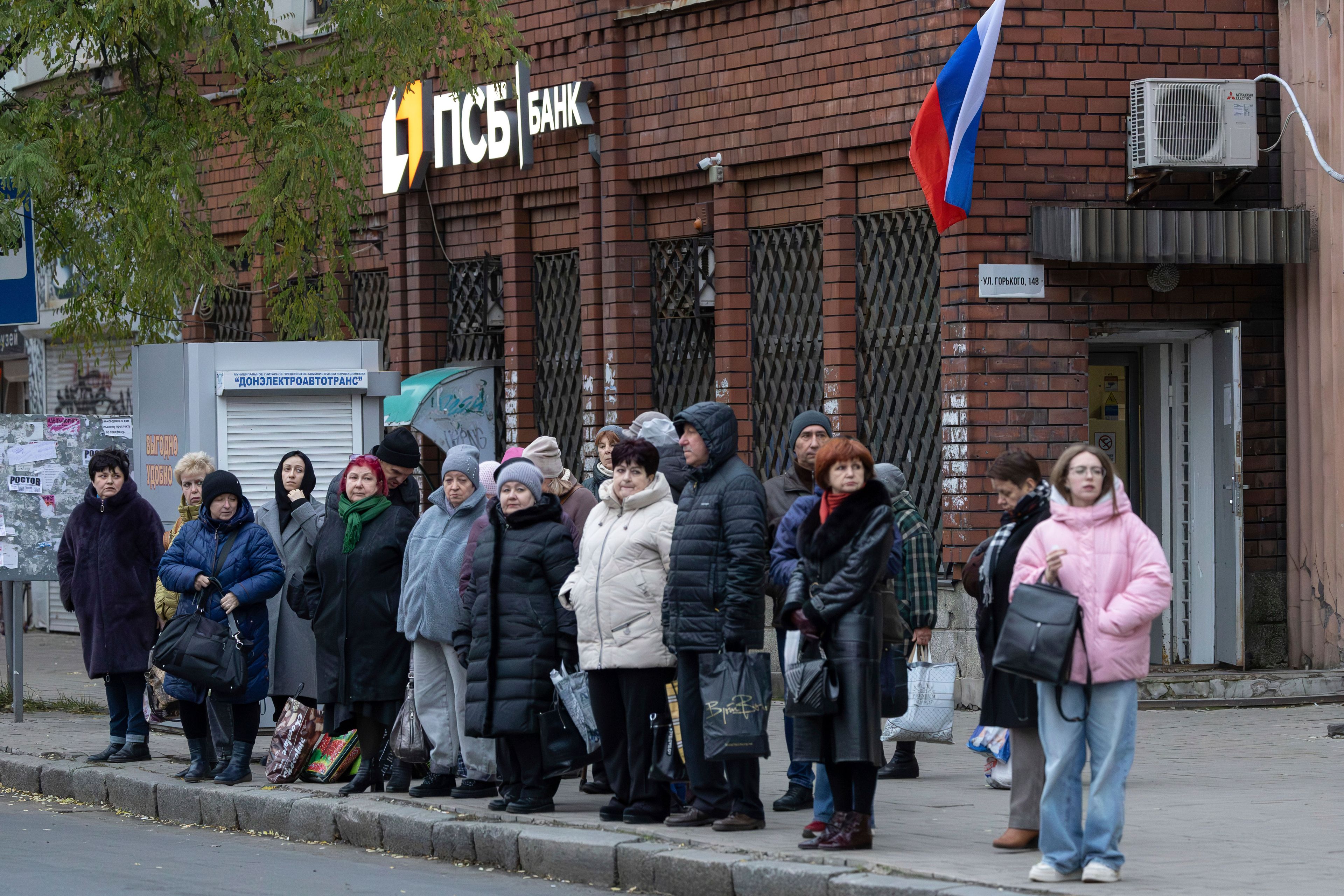 People wait at a bus stop in Donetsk, in Russian-controlled Donetsk region, eastern Ukraine, Monday, Nov. 11, 2024. (AP Photo/Alexei Alexandrov)