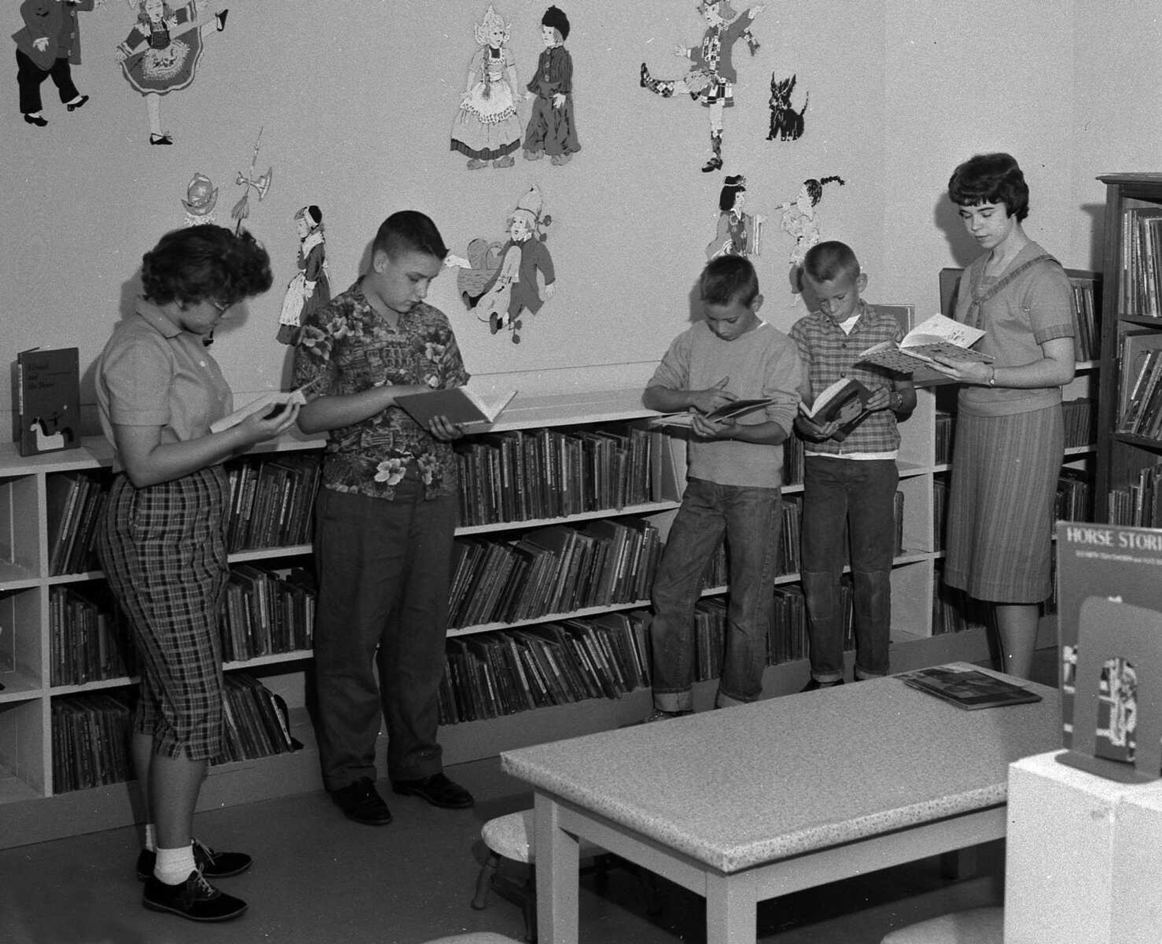 Oct. 6, 1961 Southeast Missourian.
Characters from the stories of many countries are set in mural pattern in the new children’s library at the Public Library. The library attracts a large number of children. Looking over books in the foreground are Martha Bacon, Donald Hellwege, Hollis Headrick and David Headrick, while the librarian, Miss Peggy Kearney, helps the youngsters in their book selections. (G.D. Fronabarger/Southeast Missourian archive)