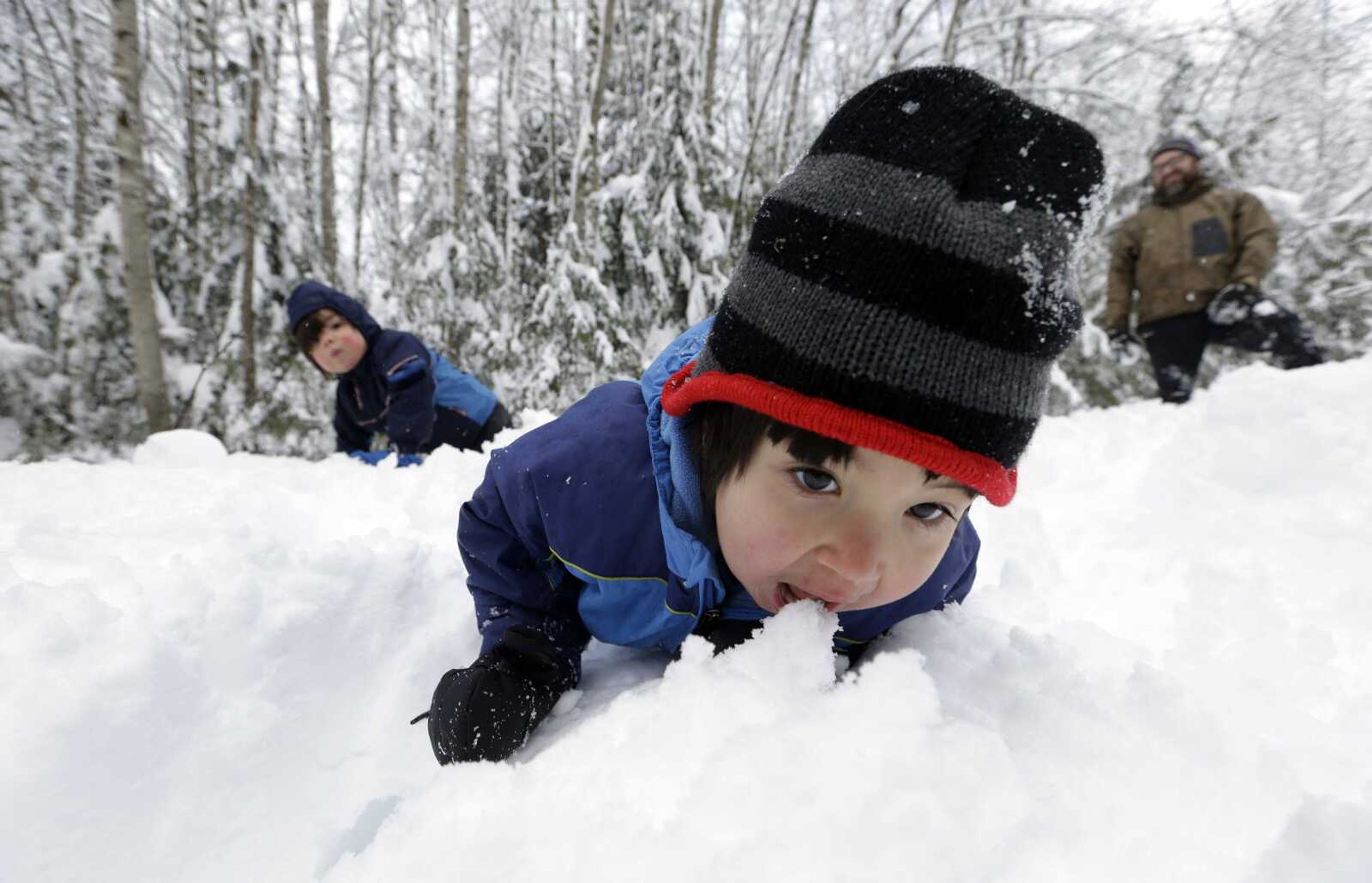 Leon Perkins, 3, leans forward to take a bite of snow as he plays with his brother Conner, left, 2, and his father Erin, on Tuesday at Snoqualmie Pass, Washington. The Seattle family headed to the mountains Tuesday to enjoy the new snow that fell overnight. But on Christmas Day, it could be warmer in New York City than Los Angeles. (Elaine Thompson ~ Associated Press)