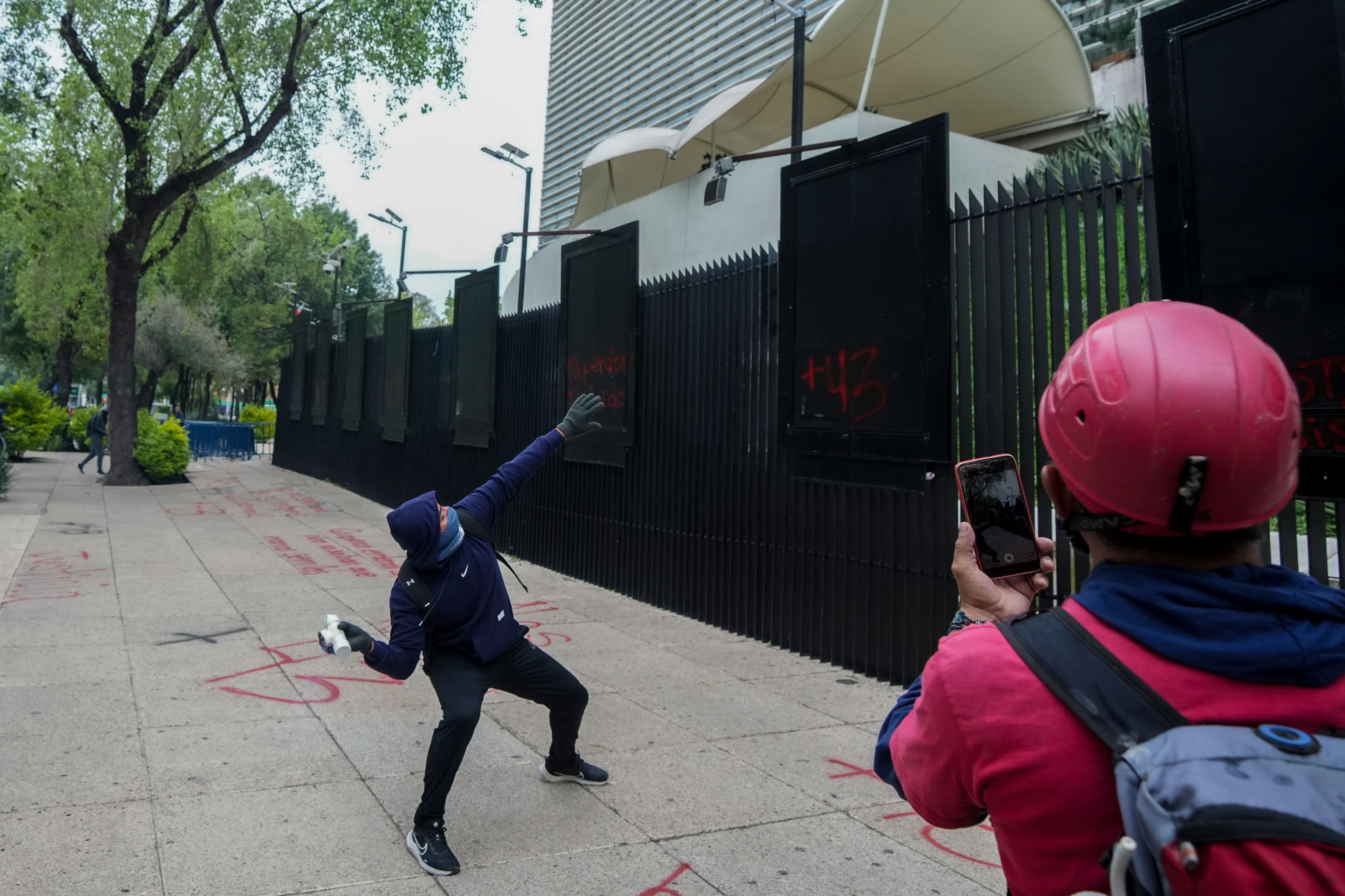 A hooded student throws an explosive at the Senate during demonstrations ahead of the 10th anniversary of the disappearance of 43 Ayotzinapa students in Guerrero state, in Mexico City, Tuesday, Sept. 24, 2024. (AP Photo/Fernando Llano)