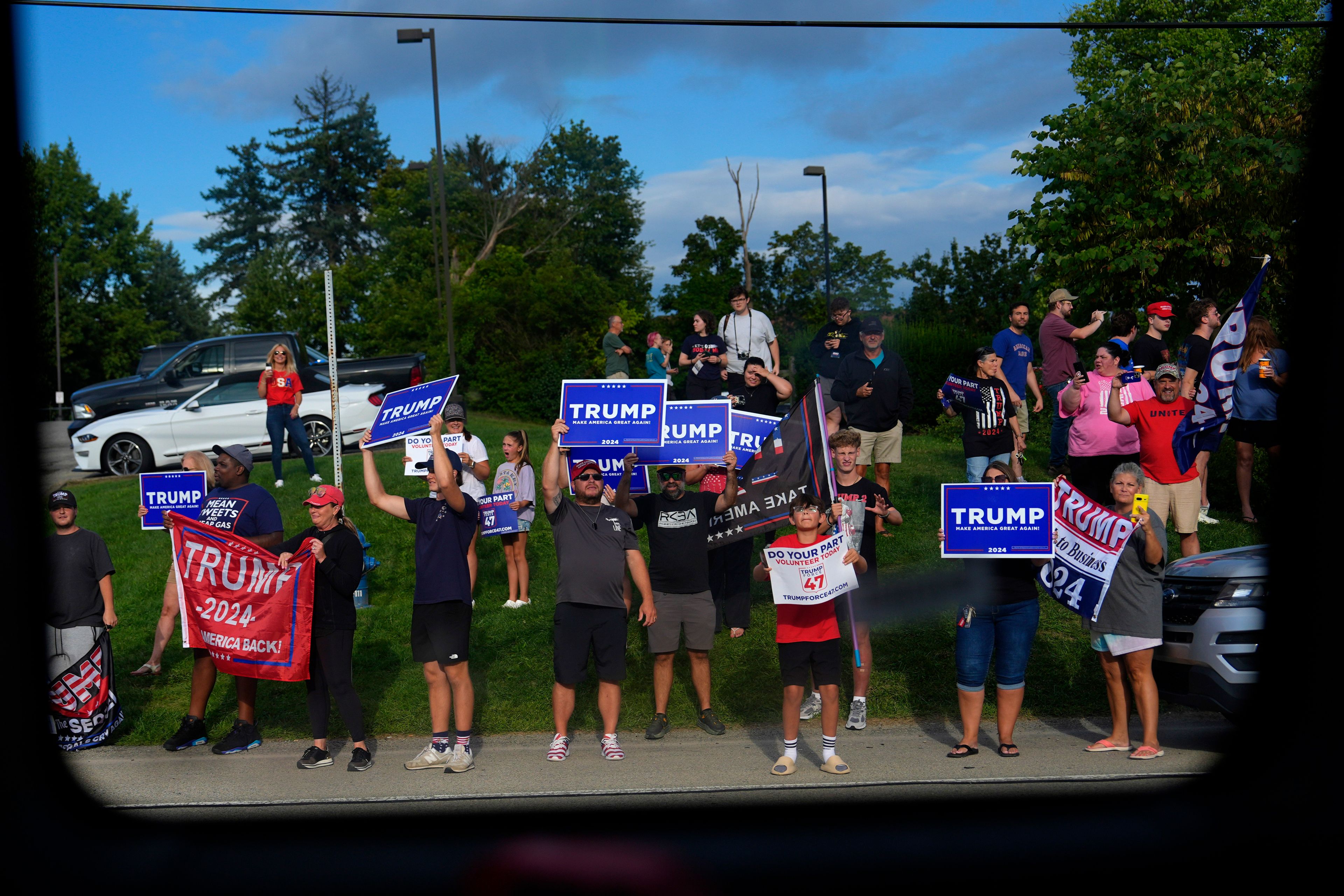 Supporters of Republican presidential candidate former President Donald Trump hold signs as Democratic presidential nominee Vice President Kamala Harris passes by on her bus en route to a campaign stop at the Primanti Bros. restaurant in Pittsburgh, on Aug. 18, 2024. (AP Photo/Julia Demaree Nikhinson)