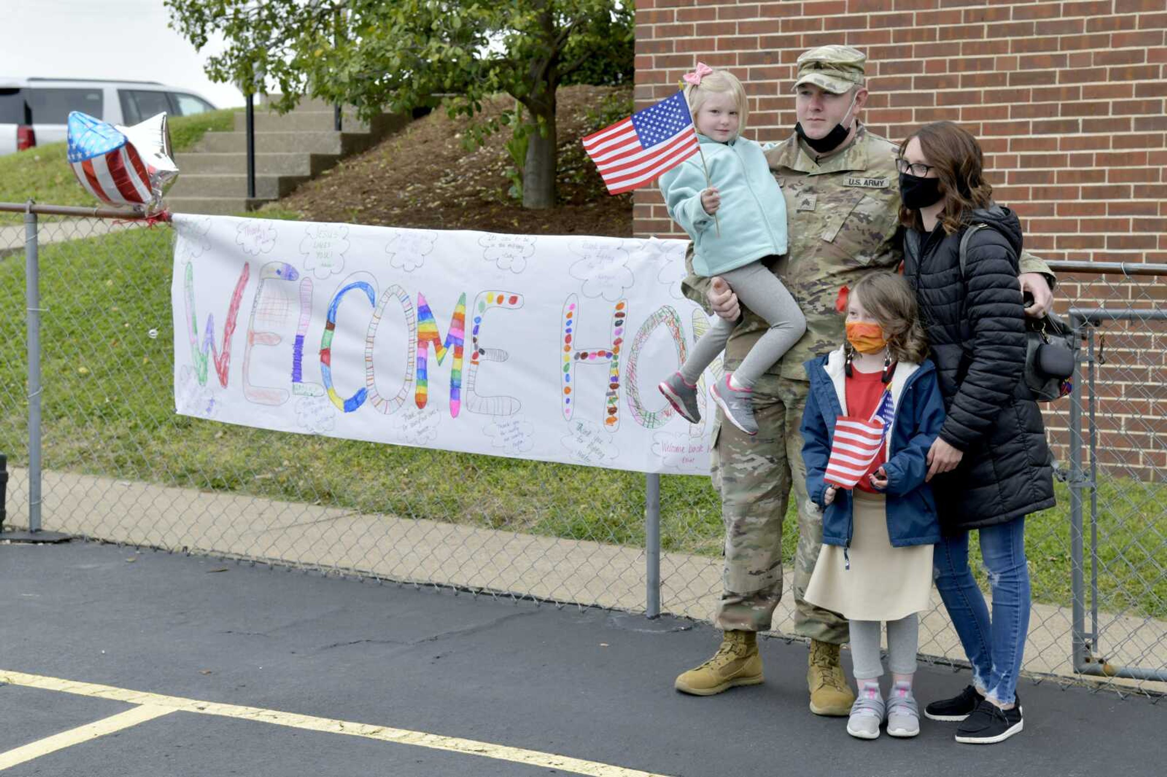 Sgt. Carl Lathum poses for a photo with his wife, Jennifer Lathum, and children, Kingsley (standing)and Ella near a welcome home sign during his surprise visit at St. Paul Lutheran School in Jackson on Friday.