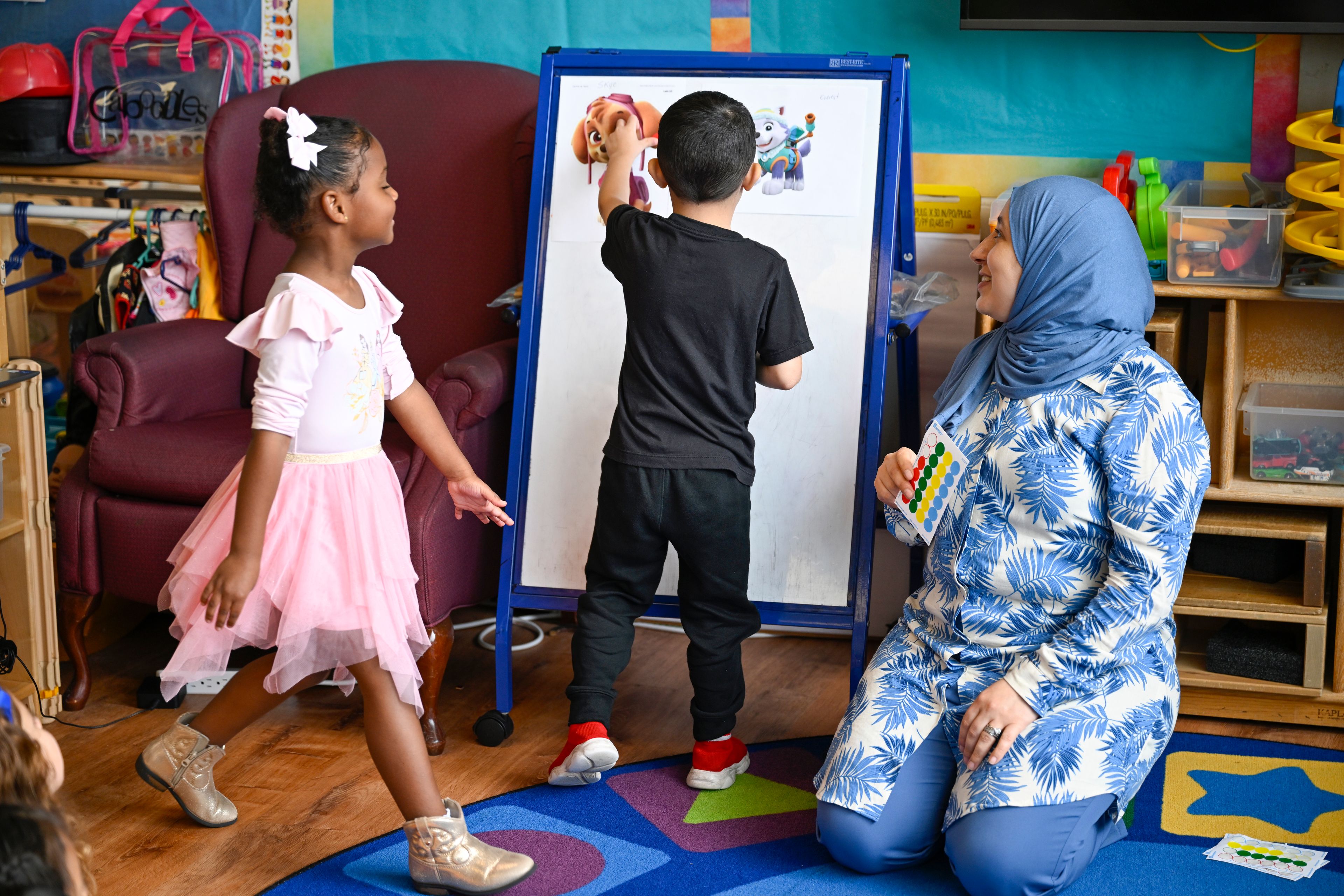 Preschool teacher Tinhinane Meziane, right, watches her students vote the most popular character of the TV show PAW Patrol at the ACCA Child Development Center, Thursday, Sept. 19, 2024, in Annandale, Va. The students are getting foundational lessons on how to live in a democracy by allowing them to regularly vote on different things through out the day. (AP Photo/John McDonnell)