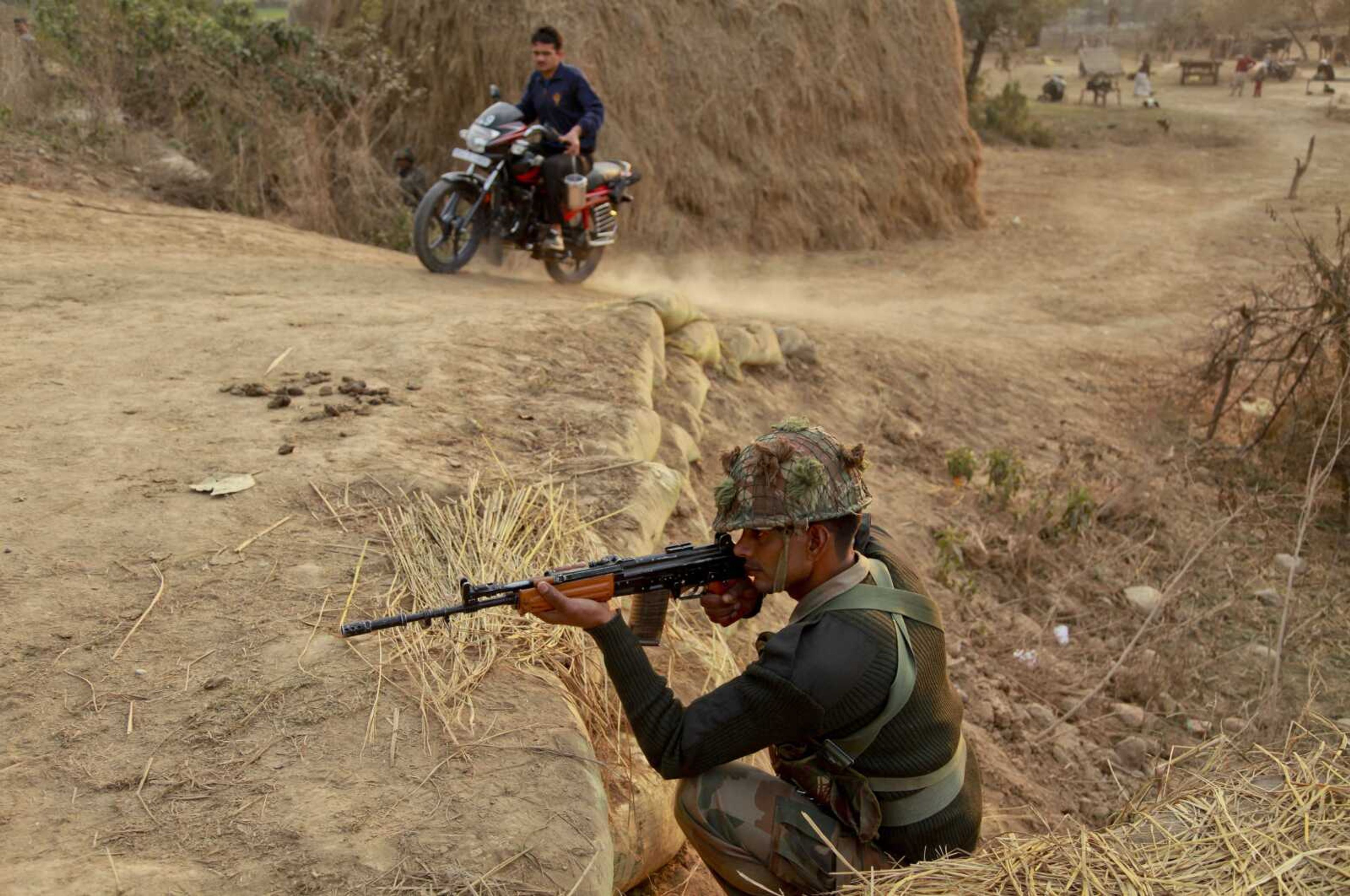 An civilian rides past as an army soldier takes position Sunday near an air base in Pathankot, India. (Channi Anand ~ Associated Press)