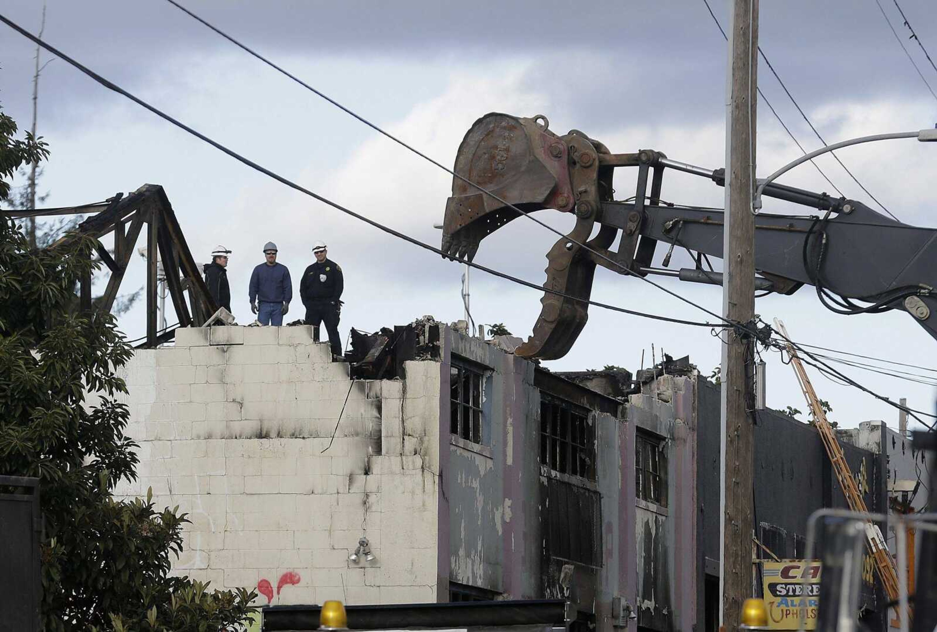 Emergency-crew workers watch as a vehicle picks up debris Tuesday at the site of a warehouse fire in Oakland, California. The fire erupted Friday, killing dozens.