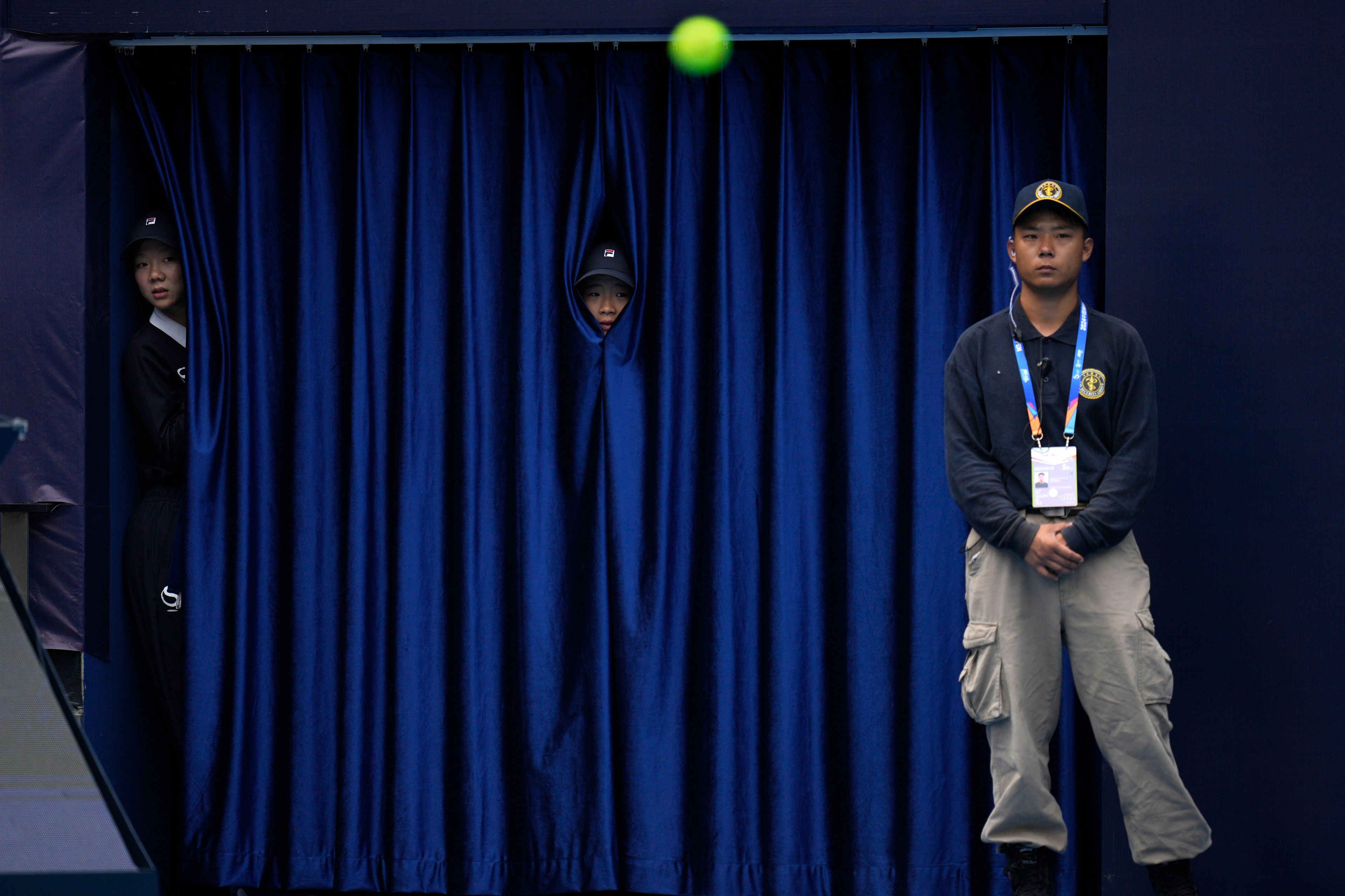 Workers peep through curtains to watch a match between France's Gael Monfils and Russia's Daniil Medvedev during the China Open tennis tournament held at the National Tennis Center in Beijing, Friday, Sept. 27, 2024. (AP Photo/Ng Han Guan)