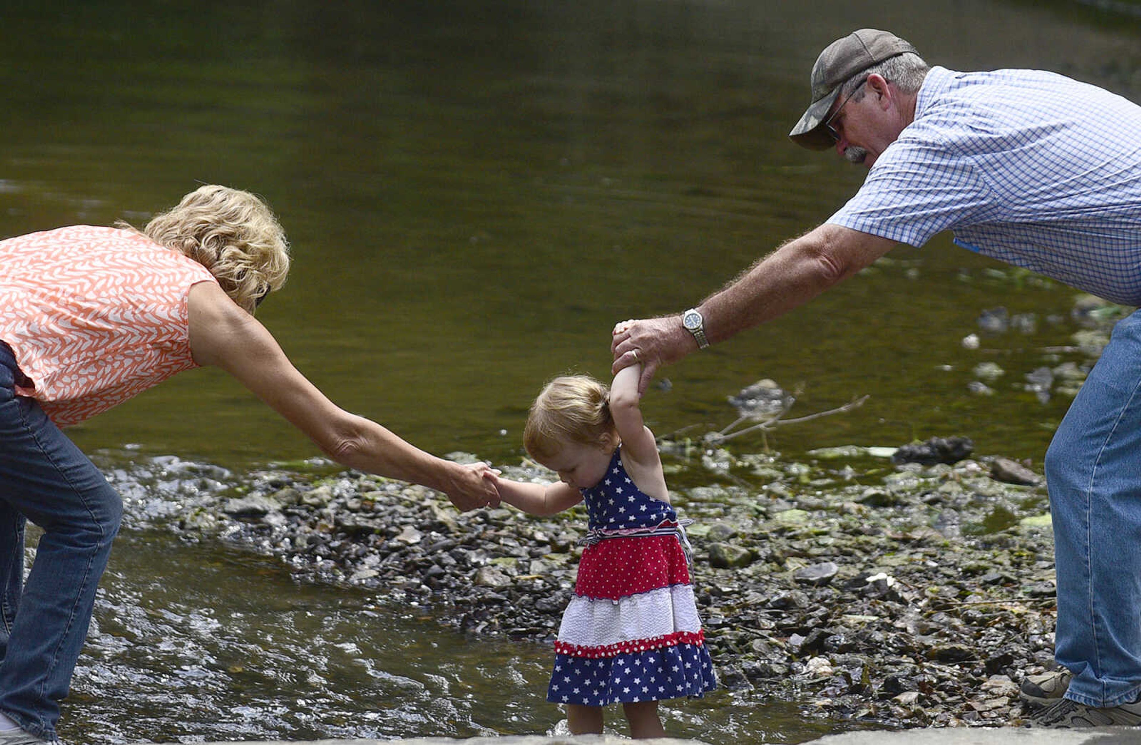 Judy and Rodney Smith hold on to their granddaughter, Charlotte Stearns, as she crosses Hubble Creek during the Fourth of July celebration on Tuesday at Jackson City Park.