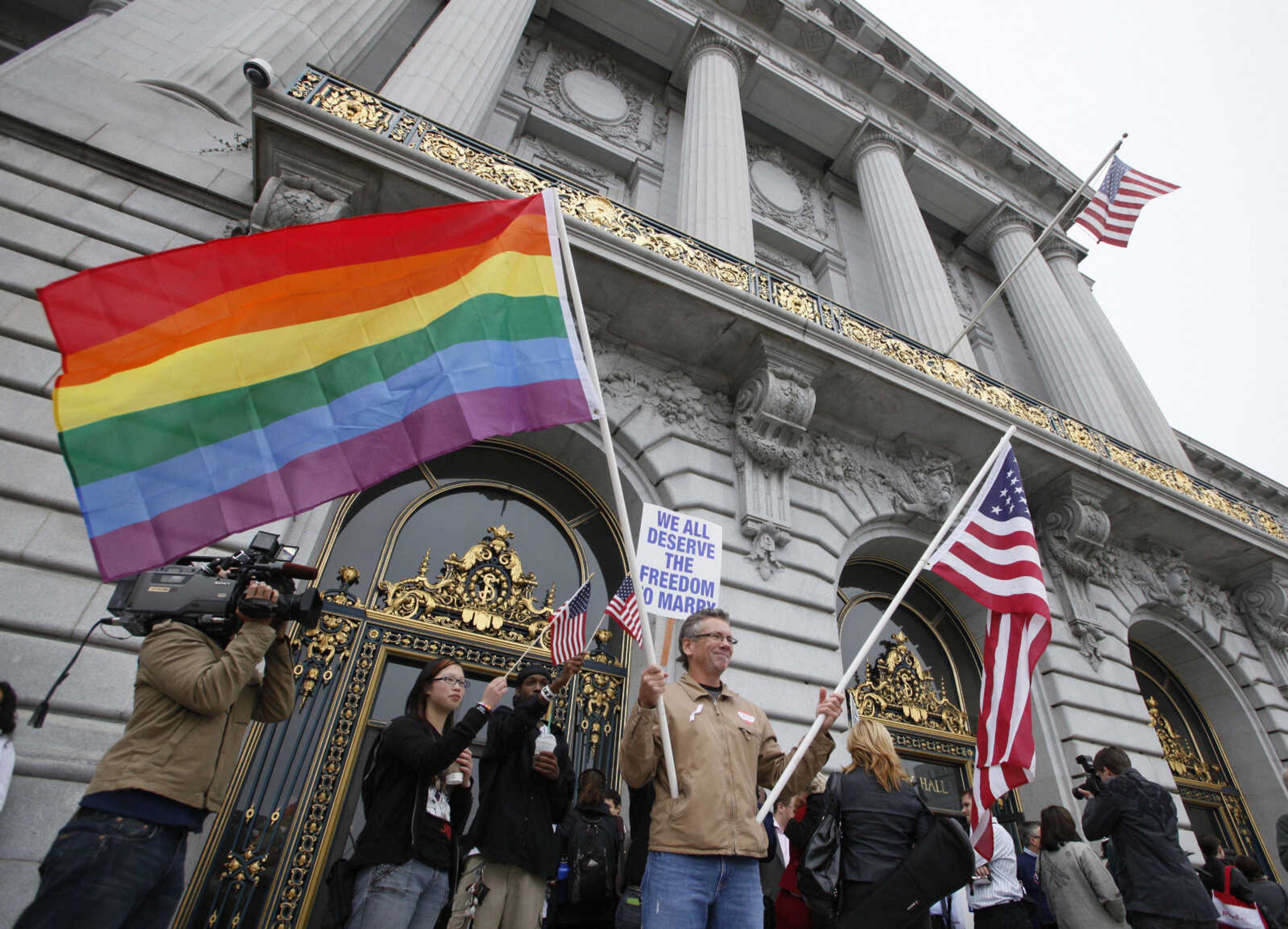 FILE - In this Aug. 12, 2010 file photo, Billy Bradford of Castro Valley, Calif., waves a pair of flags outside City Hall while same-sex couple line up to see if they can be married in San Francisco, Thursday, August 12, 2010. (AP Photo/Eric Risberg, File)