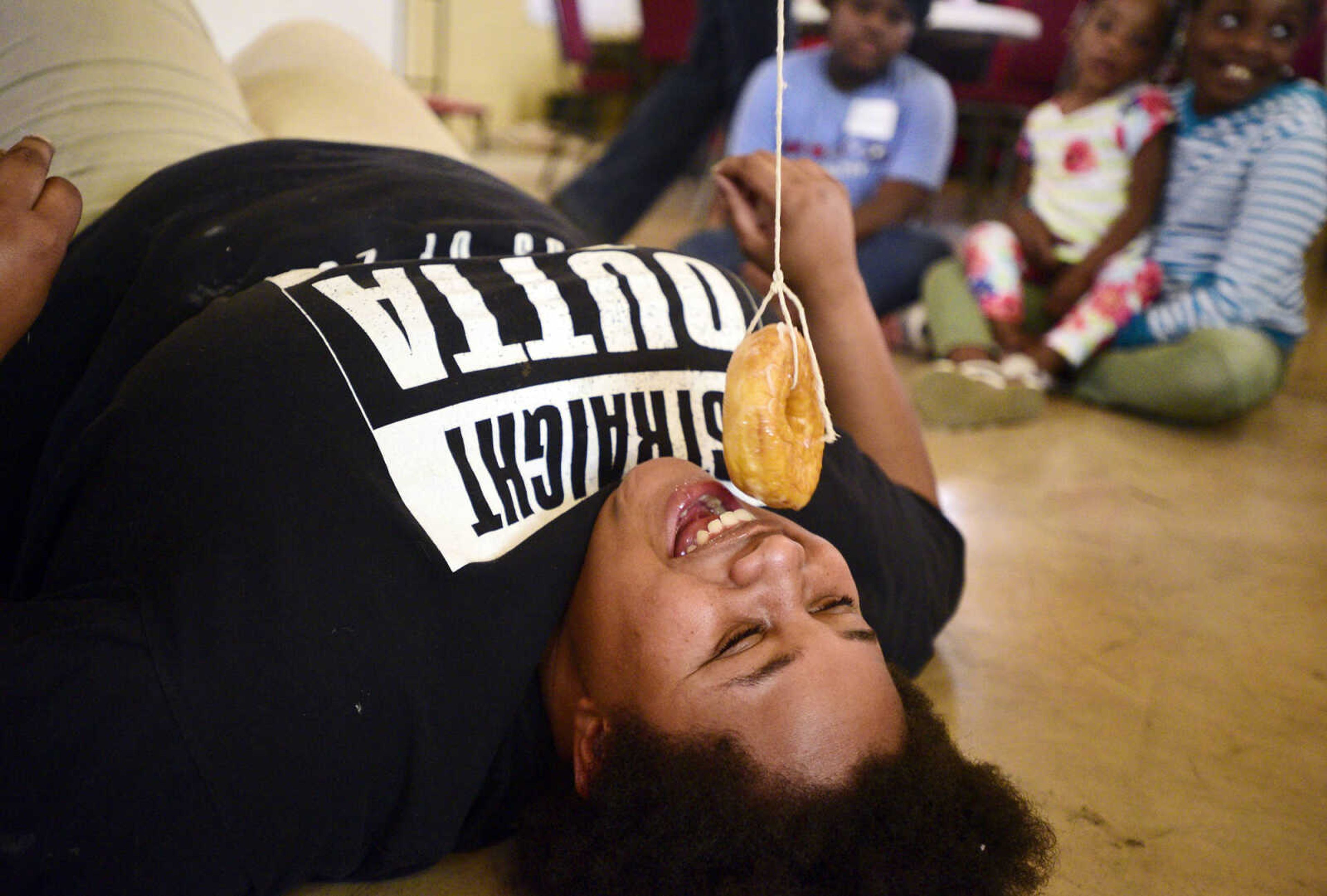 Cherish Moore tries eating a donut that her sister Chamika is dangling above her on Monday, Aug. 14, 2017, during the Salvation Army's after school program at The Bridge Outreach Center in Cape Girardeau.