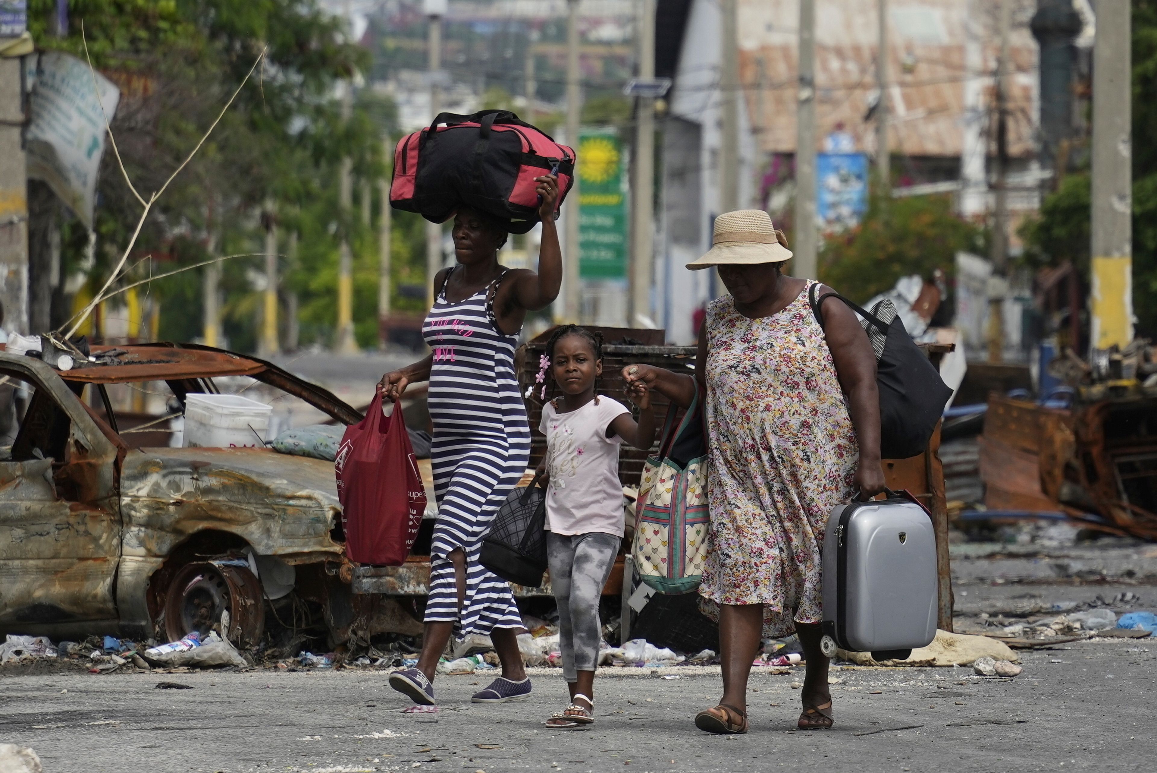 FILE - Residents walk past a burnt car blocking the street as they evacuate the Delmas 22 neighborhood to escape gang violence in Port-au-Prince, Haiti, on May 2, 2024. (AP Photo/Ramon Espinosa, File)