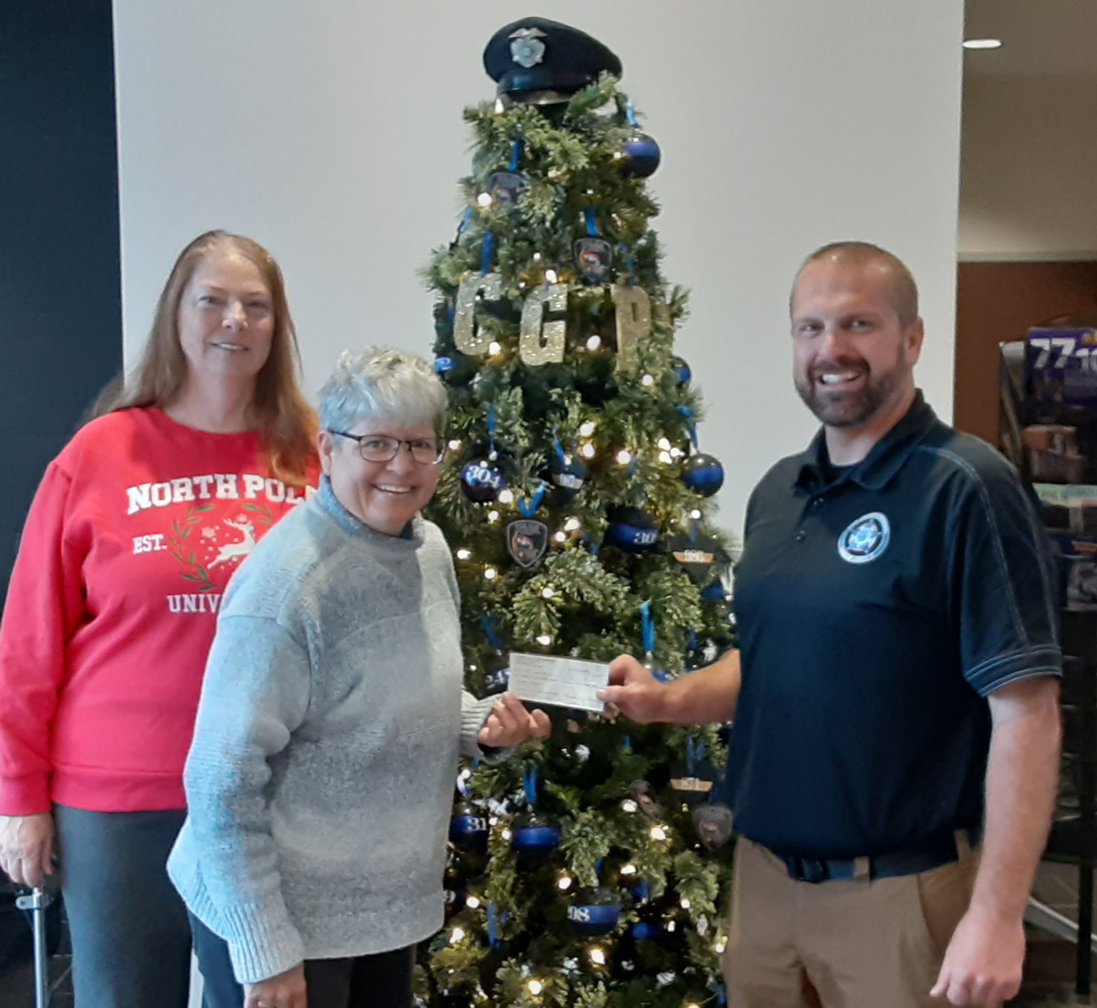 Treasa Benn and Kristin Ham of the Evening Optimists give a check for $1500 to Cpl. Johnny Spencer of Cape Fraternal Order of Police, Lodge 51 for Shop with a Hero event. Each December local heroes including law enforcement officers, fire fighters, and first responders shop with needy children at the Cape Walmart Supercenter with funds provided by local businesses and organizations.