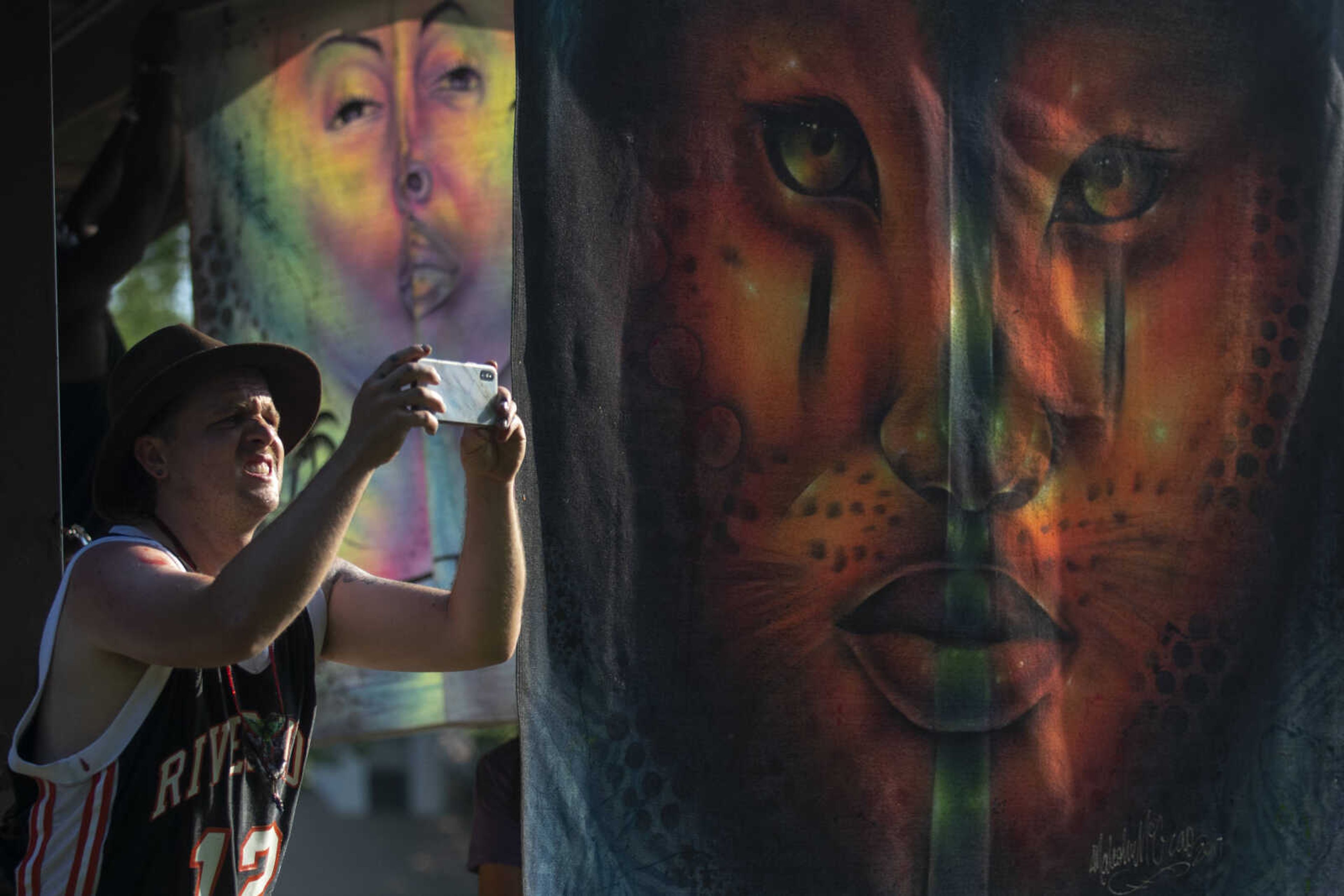 Ben Koller, originally of Milwaukee and now Asheville, North Carolina, holds up a phone near pieces of artwork during a Cape Girardeau Community Art Day on Sunday, June 30, 2019, at Ranney Park in Cape Girardeau.