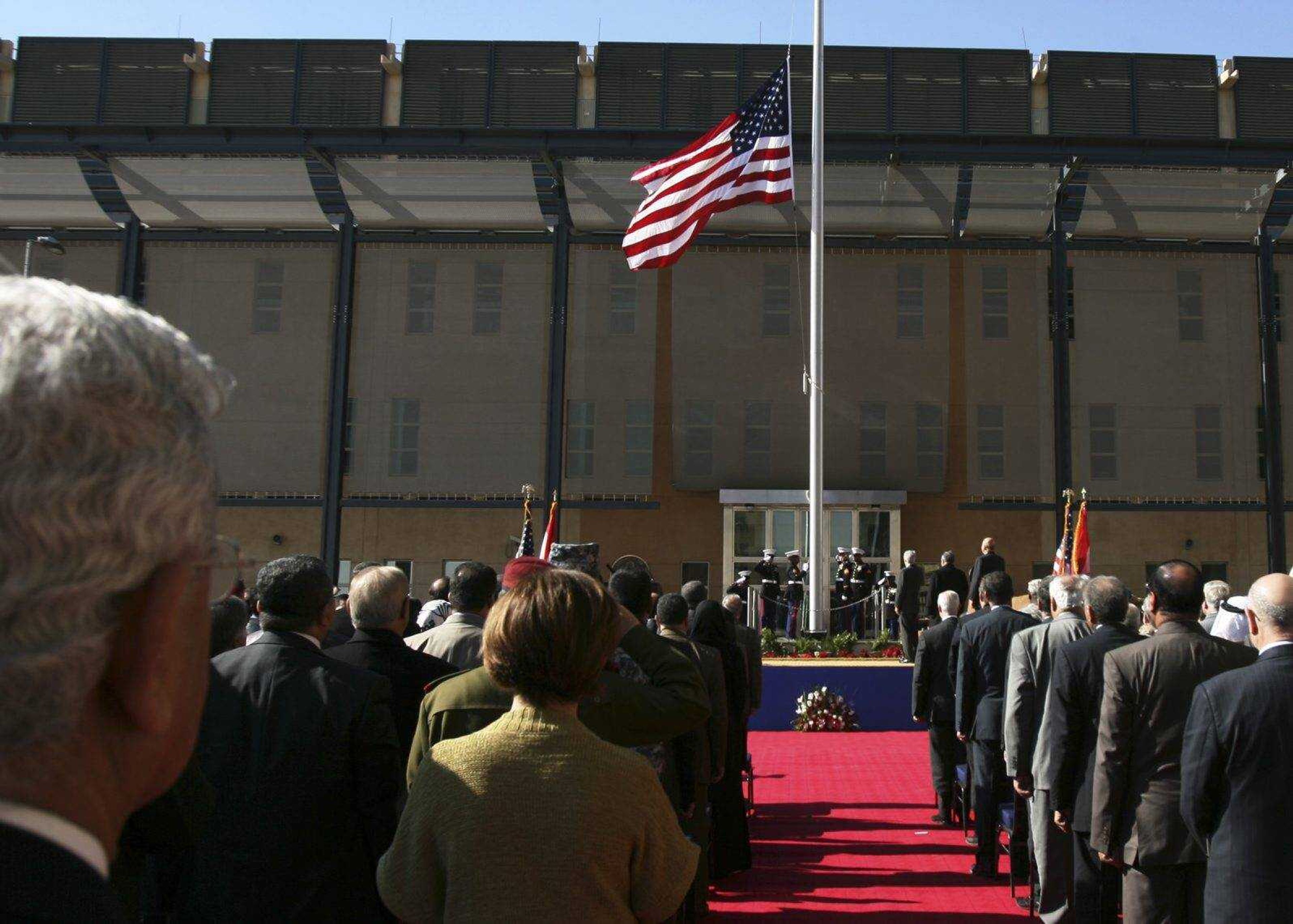 People watch the U.S. flag as it is raised during a 2009 ceremony marking the opening of the new U.S. Embassy in Baghdad. Wednesday, the U.S. Embassy in Baghdad ordered all non-essential, non-emergency government staff to leave Iraq immediately amid escalating tensions with Iran.