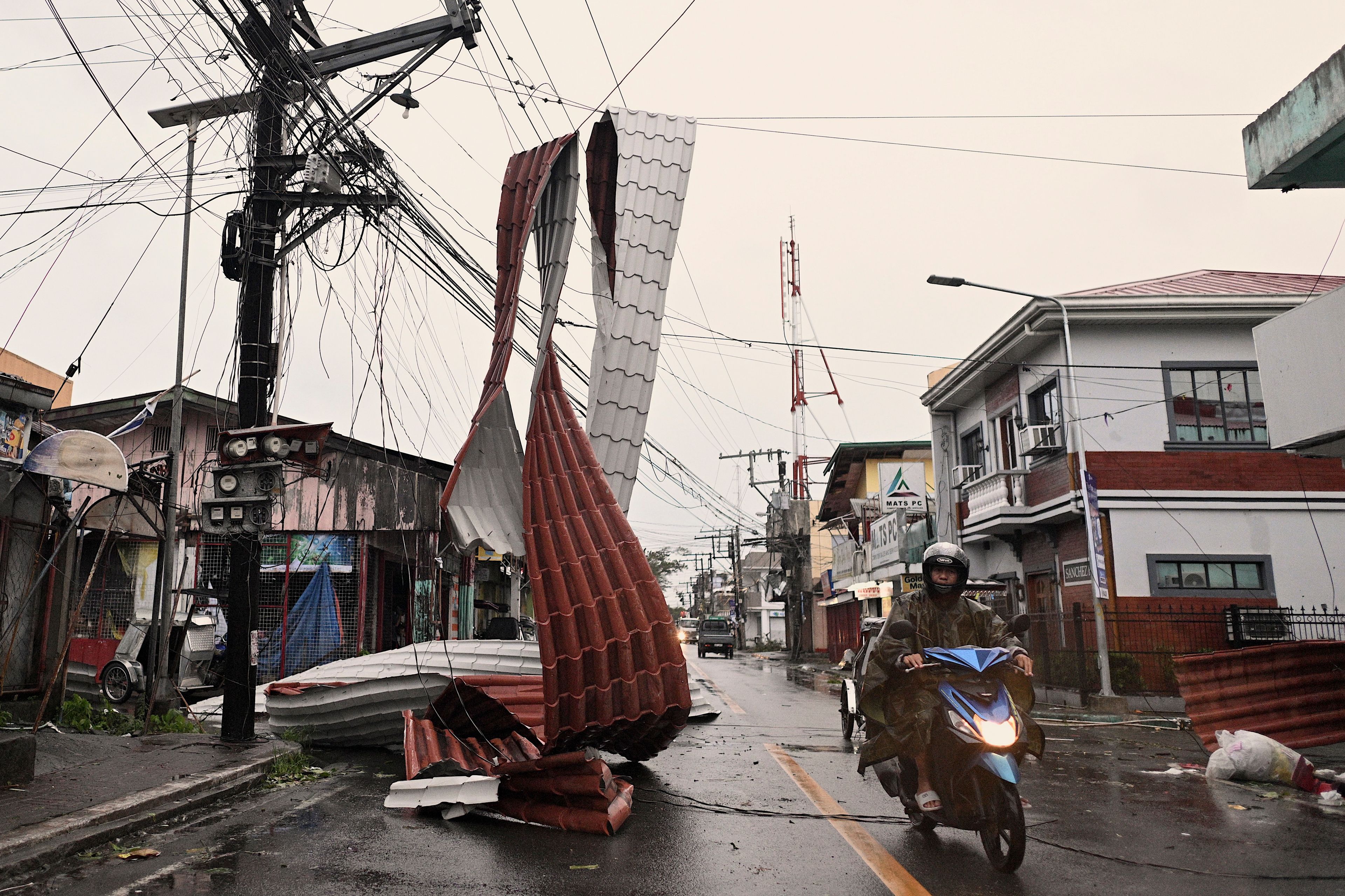 Motorists ride past a part of a roof suspended on electric wires blown by strong winds caused by Typhoon Man-yi along a street in the municipality of Baler, Aurora province, northeastern Philippines Monday, Nov. 18, 2024. (AP Photo/Noel Celis)