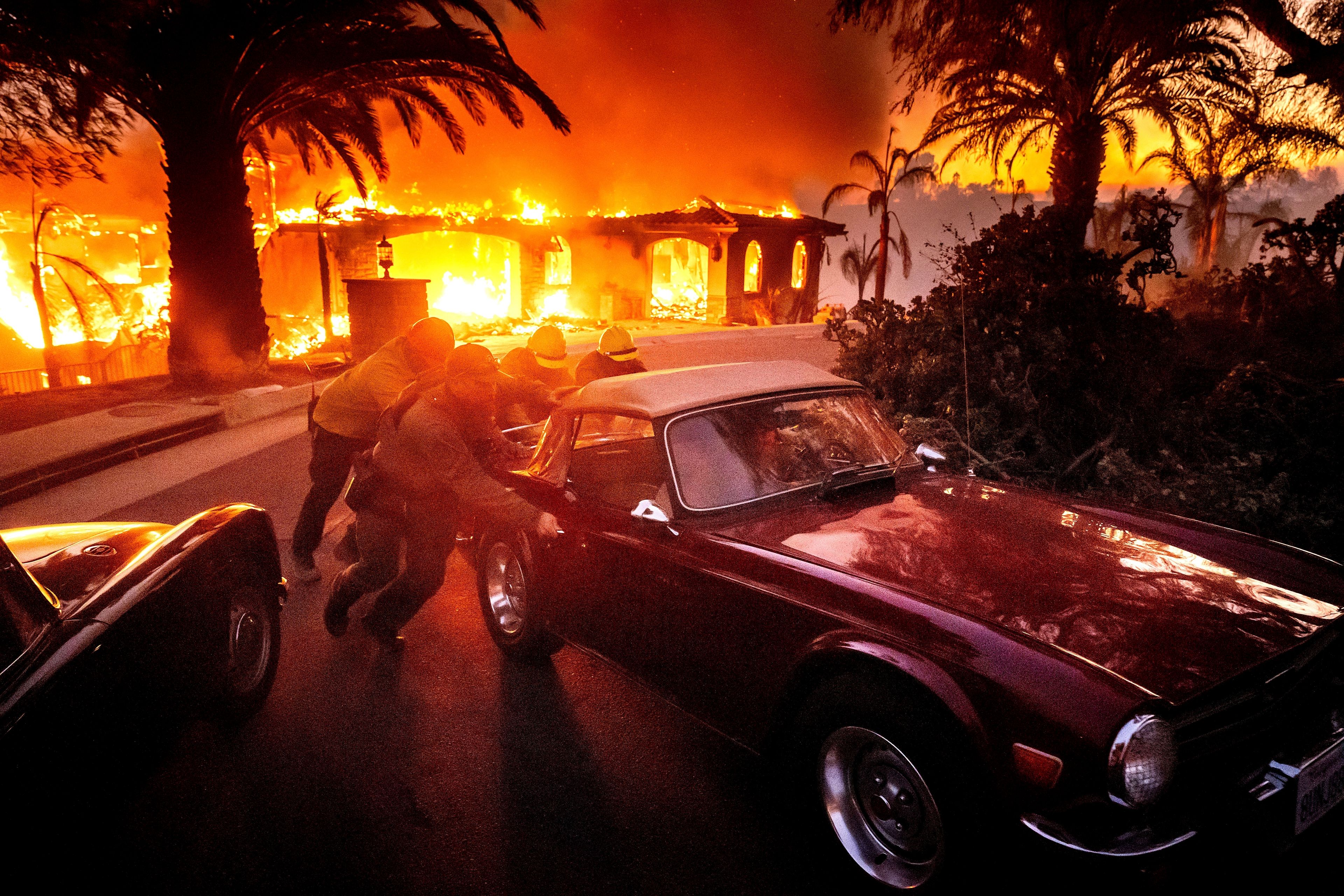 Firefighters and sheriff's deputies push a vintage car away from a burning home as the Mountain Fire burns in Camarillo, Calif., Nov. 6, 2024. (AP Photo/Noah Berger)