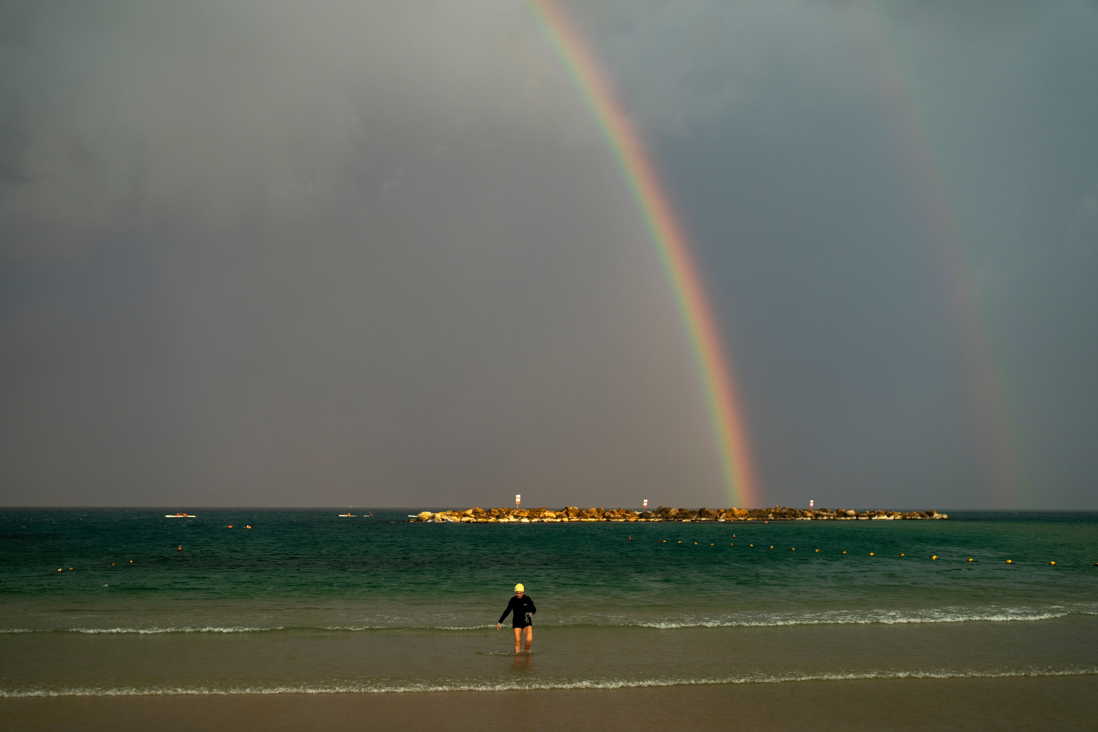 A rainbow stretches across the sky as a woman walks along the shore after swimming at the Mediterranean sea, in Tel Aviv, Israel, Monday, Nov. 4, 2024. (AP Photo/Francisco Seco)