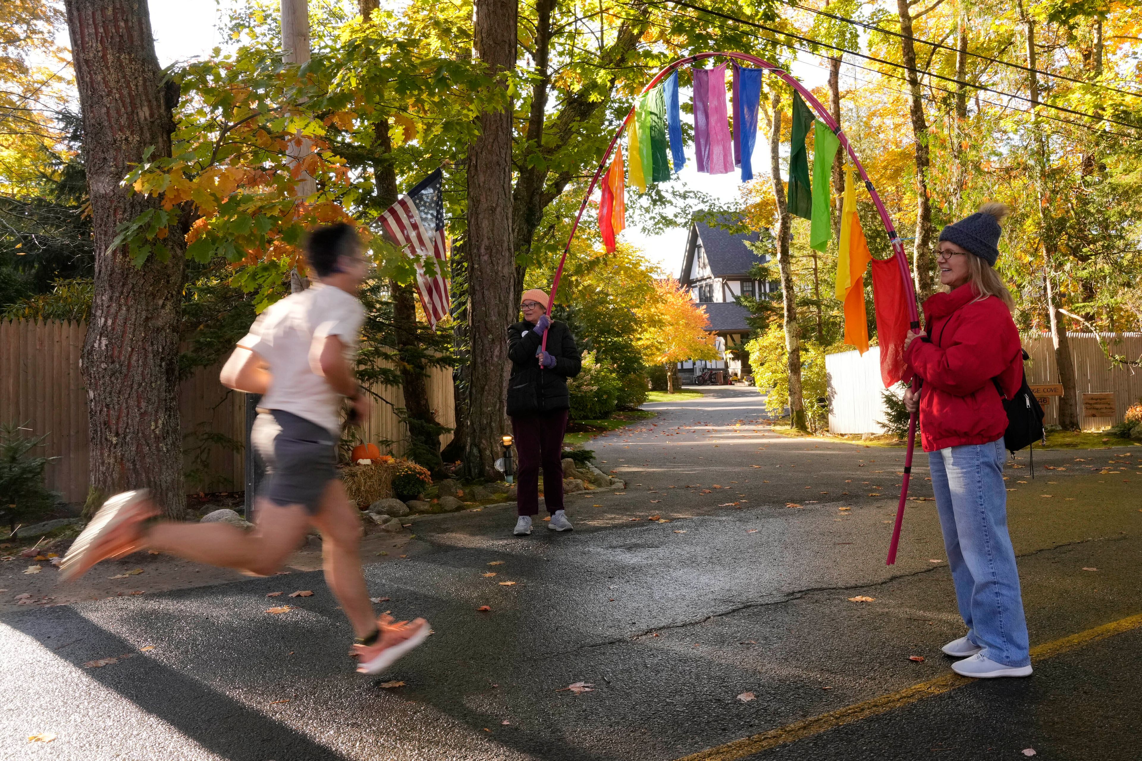 A runner passes by people protesting in front of the home of Leonard Leo during the Mount Desert Island Marathon, Sunday, Oct. 20, 2024, in Northeast Harbor, Maine. (AP Photo/Robert F. Bukaty)