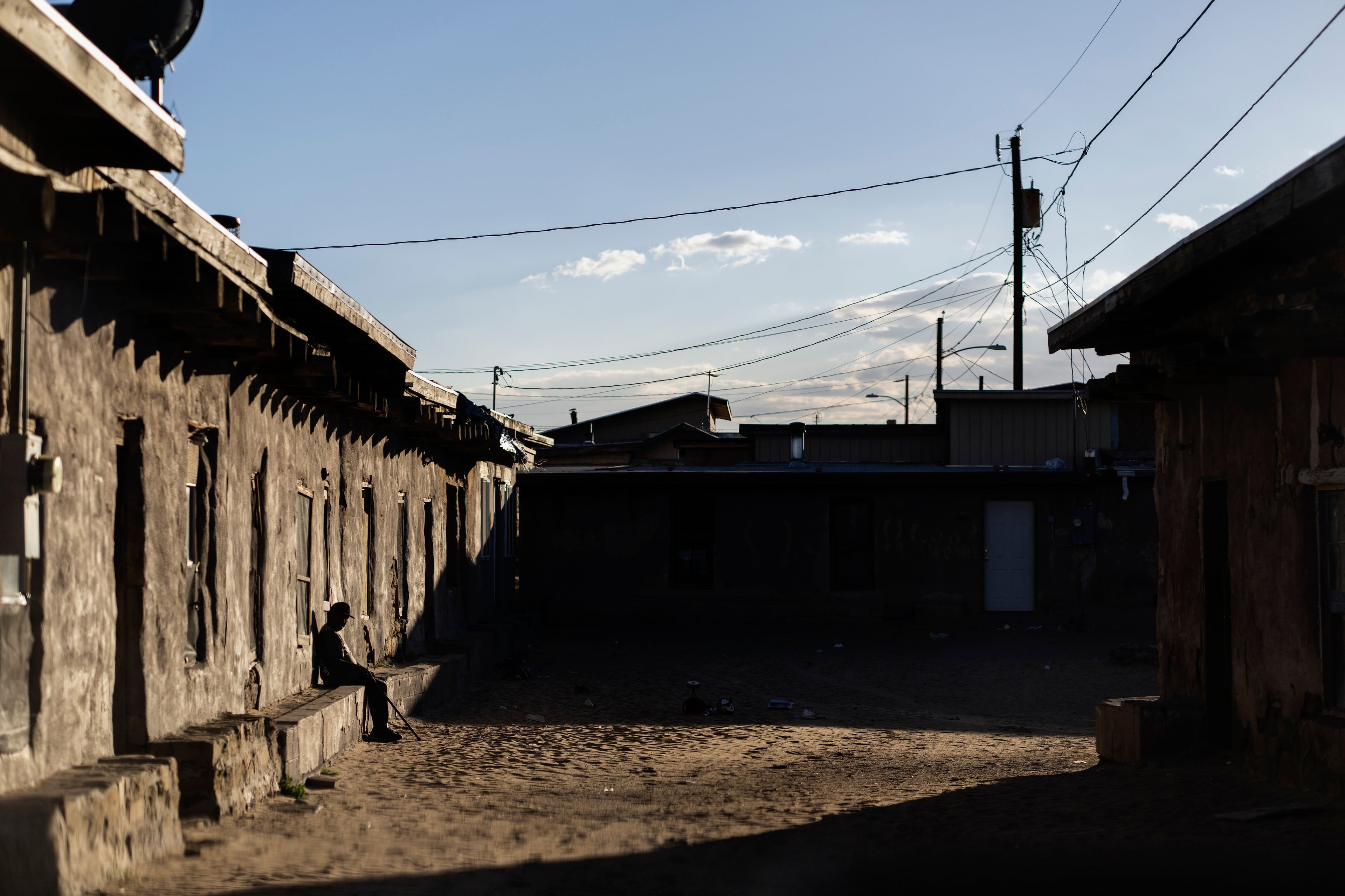 A Hopi man warms himself in the sun while sitting against an adobe building, in Sichomivi, Ariz., Wednesday, Oct. 16, 2024. (AP Photo/Rodrigo Abd)