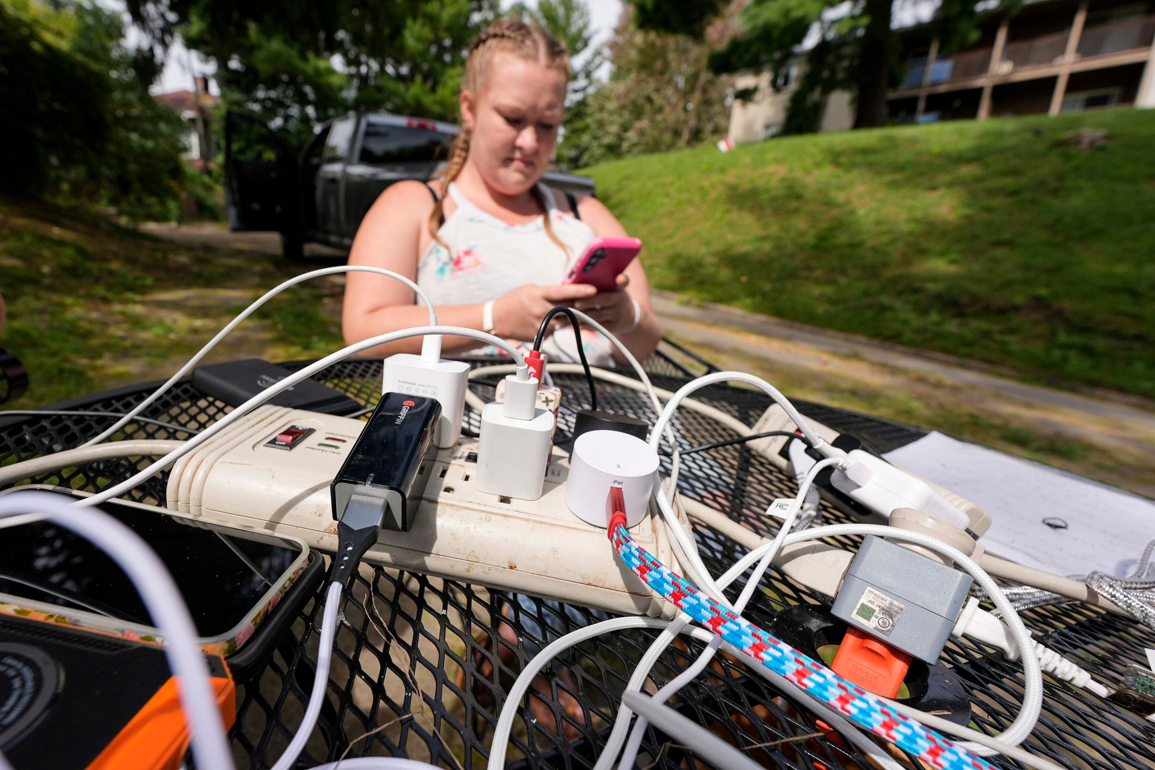 Carrie Owenby looks at her phone as a neighbor with power dropped an extension cord for neighbors who have no power in the aftermath of Hurricane Helene, Monday, Sept. 30, 2024, in Asheville, N.C. (AP Photo/Mike Stewart)