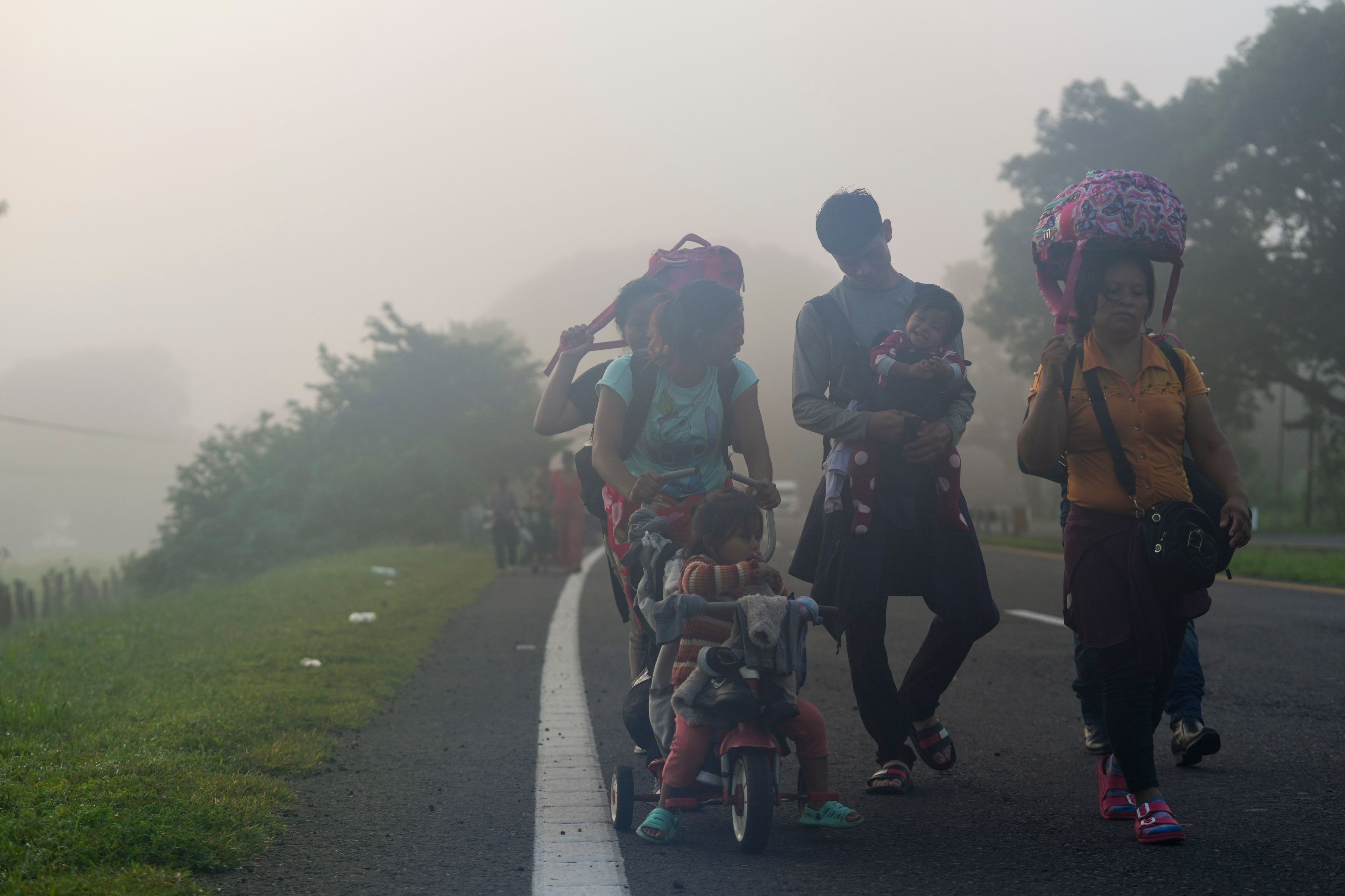 Migrants walk through the morning fog on the highway in Huixtla, southern Mexico, heading toward the country's northern border and ultimately the United States, Thursday, Nov. 7, 2024. (AP Photo/Moises Castillo)