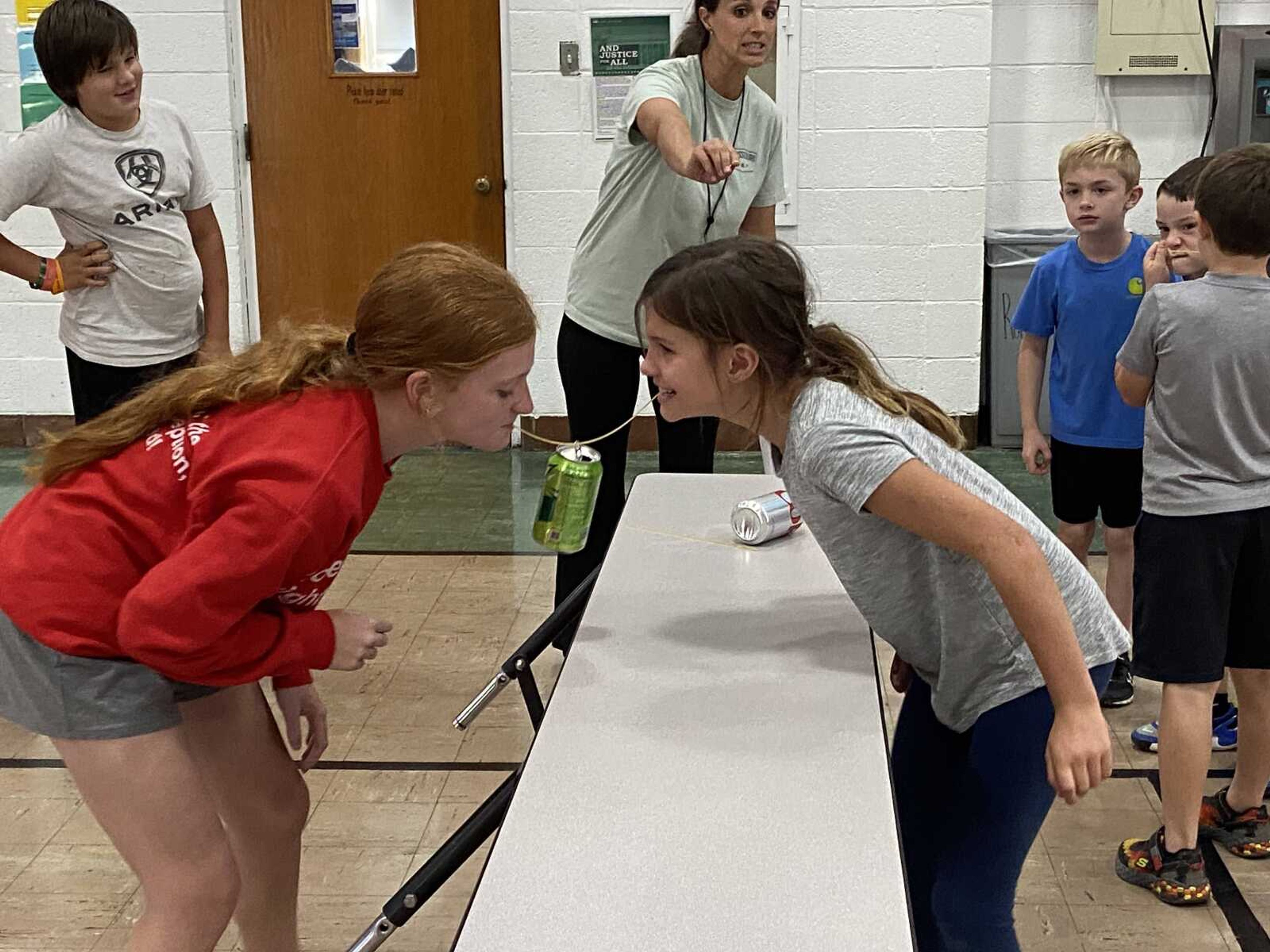 Adisyn Seabaugh & Laynie Priggel of St. Michael's house carefully carry the soda can from one end to the other, hoping to not break the spaghetti stick and have to start over.  Dylan Levan, Hannah Priggel (House monitor), Trase Webb, and Lane Seyer are hoping they can make it, too.