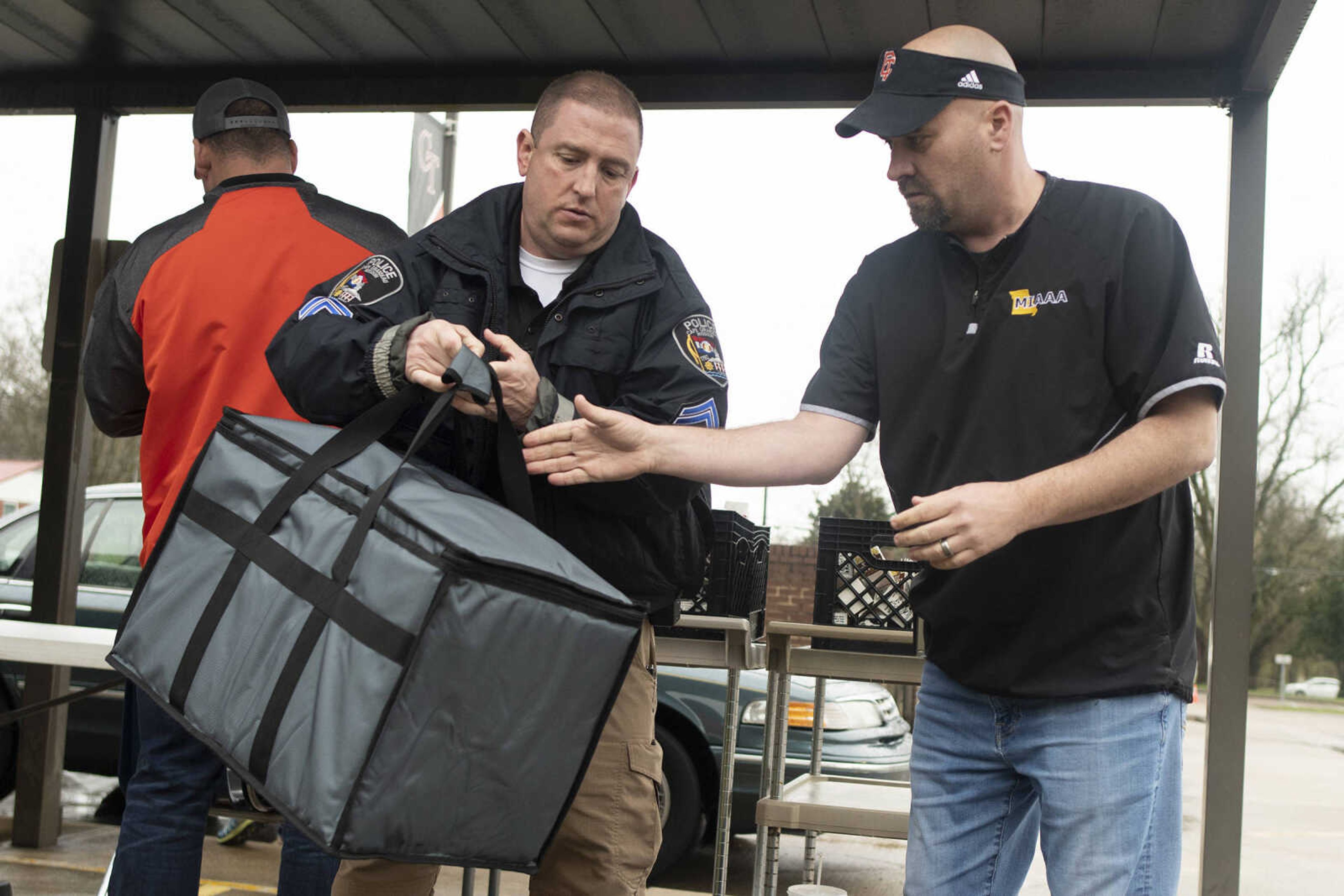 Cape Girardeau Police Department Cpl. Mark Wyatt hands a container to Cape Central High School athletic director Tyson Moyers while giving out meals for those 18 years old and younger Wednesday, March 18, 2020, at Clippard Elementary in Cape Girardeau.