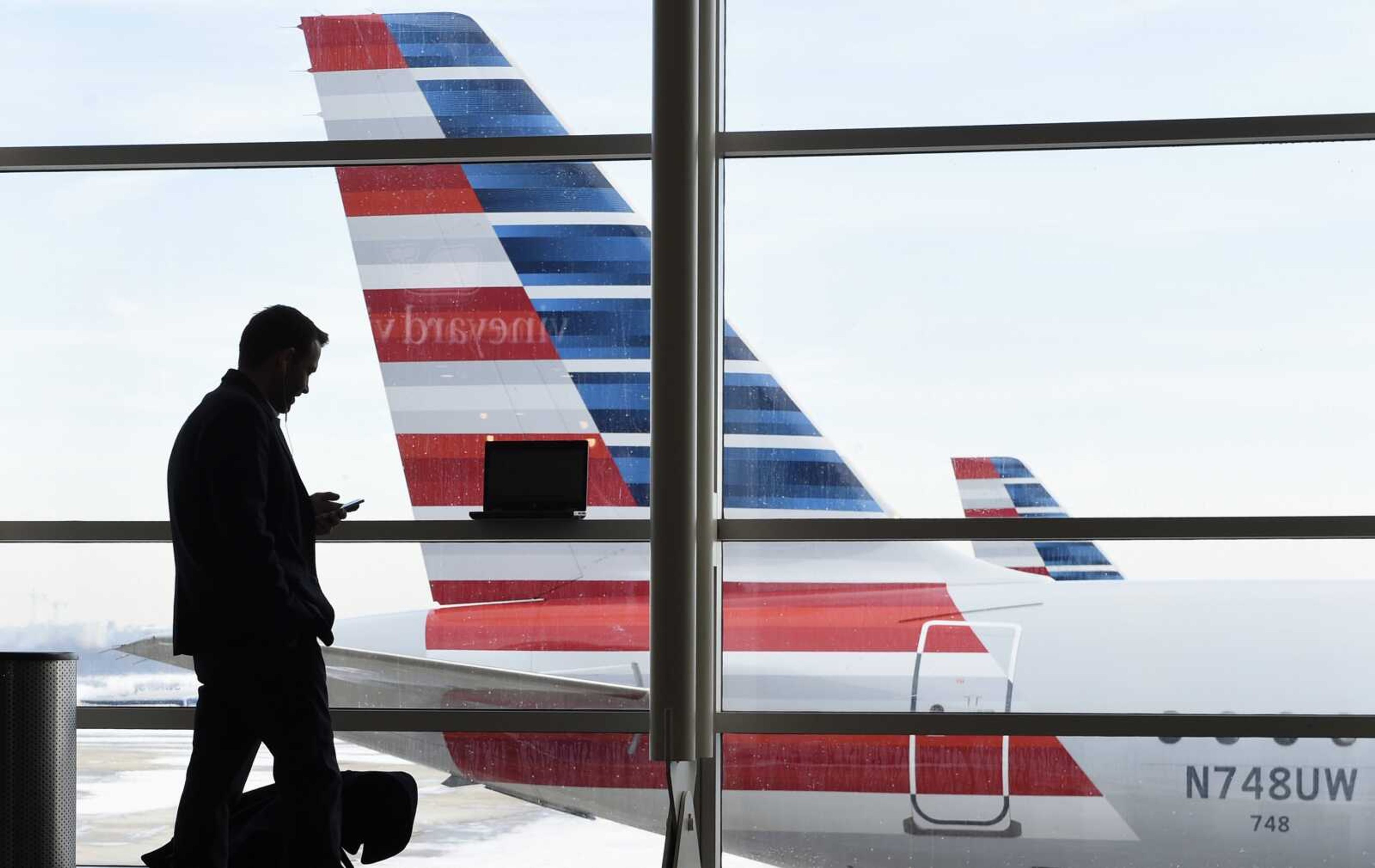 A passenger talks on the phone as American Airlines jets sit parked at their gates at Washington's Ronald Reagan National Airport. American Airlines announced passengers will be able to buy "basic economy" tickets starting in February.