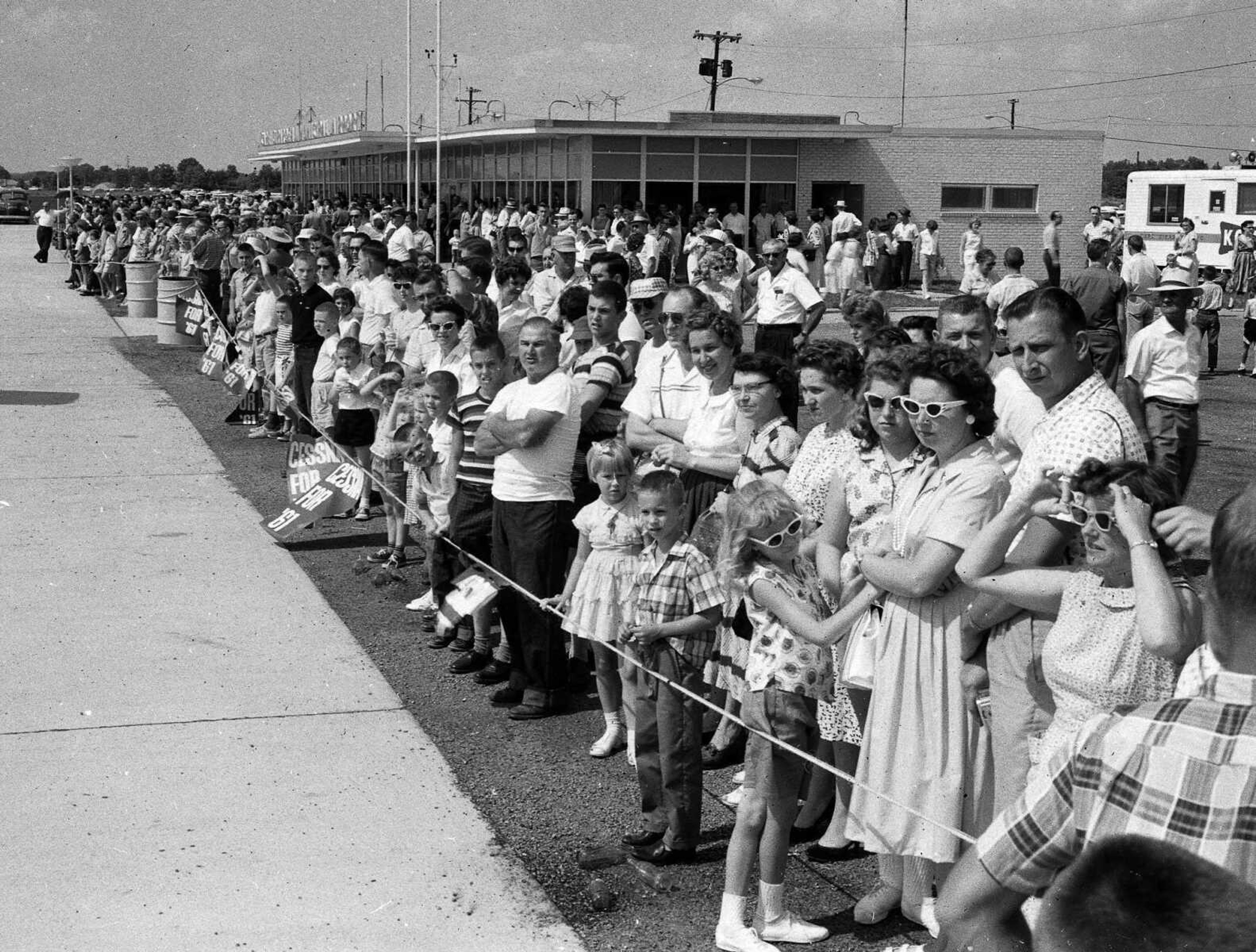 June 26, 1961 Southeast Missourian.
Aviation Day at Municipal Airport Sunday brought out what airport officials and police estimated as the largest crowd ever present at the field. The crowd, surpassing even that of the airport dedication last summer, was estimated at close to 10,000 persons. The picture shows a part of the crowd in front of and south of the new administration building watching planes arrive and leave, taking passengers for rides over the city and seeing parachute jumps staged by the Mau Mau Sports Parachute Club of Cape and the Greater St. Louis Parachute Club, and other events which all day long entertained the visitors. (G.D. Fronabarger/Southeast Missourian archive)