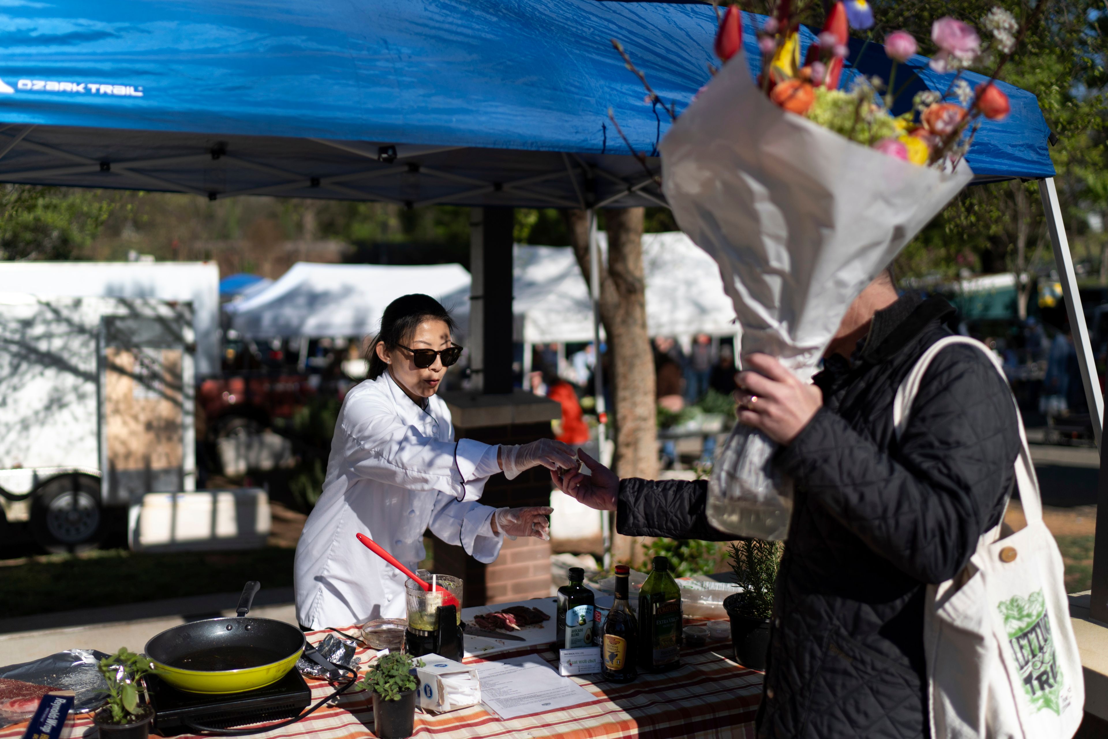 Dee Iraca, left, who was adopted as a baby out of South Korea to a family in the United States, works as chef at a farmer's market Saturday, April 6, 2024, in Davidson, N.C. Iraca and her twin sister are now taking care of their adoptive mother, who has health challenges and it's difficult to find the time and money to visit South Korea. But they want to make the effort to get to know their father. (AP Photo/David Goldman)