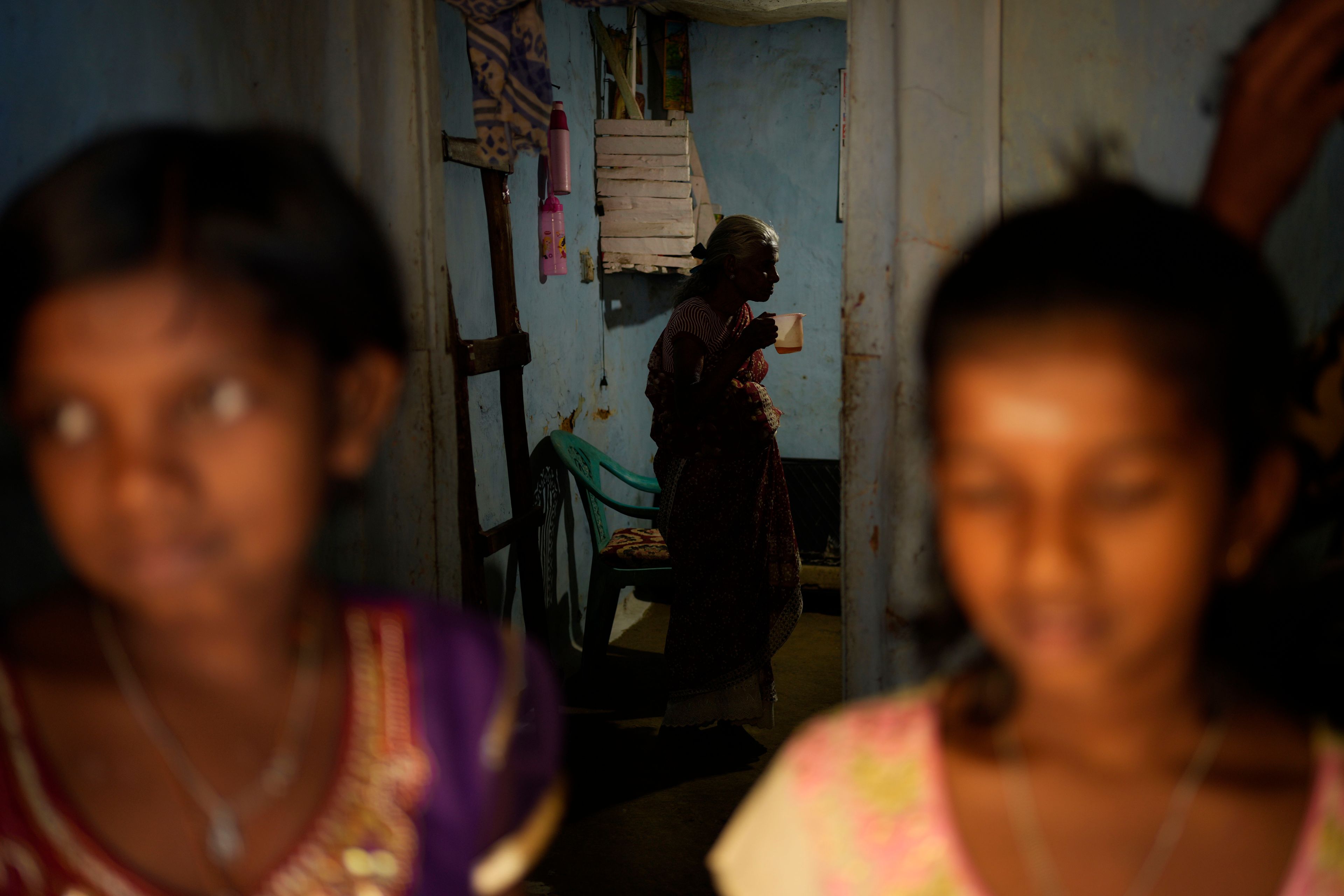 The twin daughters of Muthuthewarkittan Manohari, a tea plantation worker, stand in the foreground as their grandmother Lakshmi, center, drinks a cup of tea in their home in Spring Valley Estate in Badulla, Sri Lanka, Tuesday, Sept. 10, 2024. (AP Photo/Eranga Jayawardena)