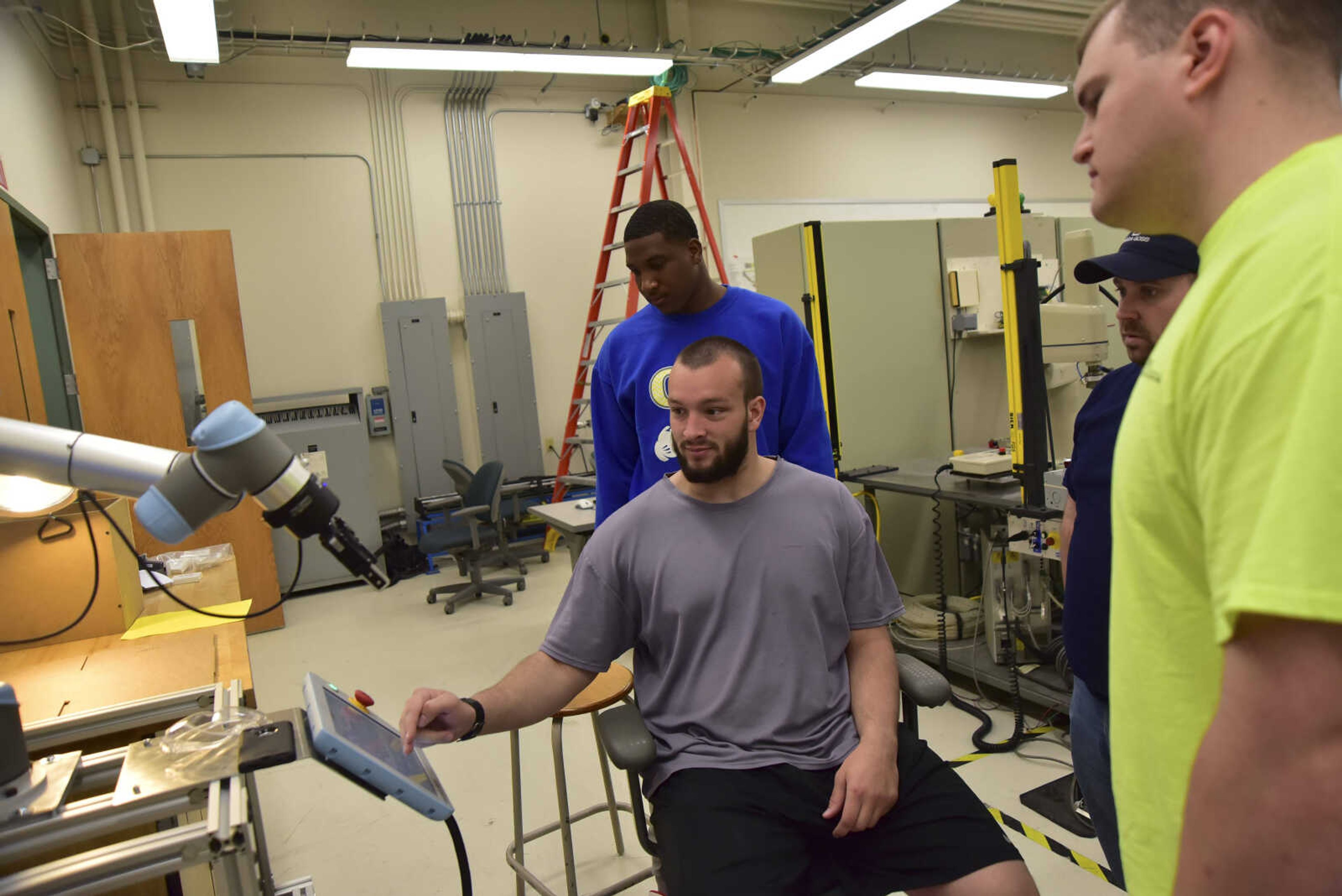 Billy Dasher sitting down at the control station and his group, Keldon Warfield, Michael Mayor and Jason Beard, transfer parts from one table to another with a robotic arm during class in the Advanced Manufacturing Lab on Thursday at the Polytech building at Southeast Missouri in Cape Girardeau.