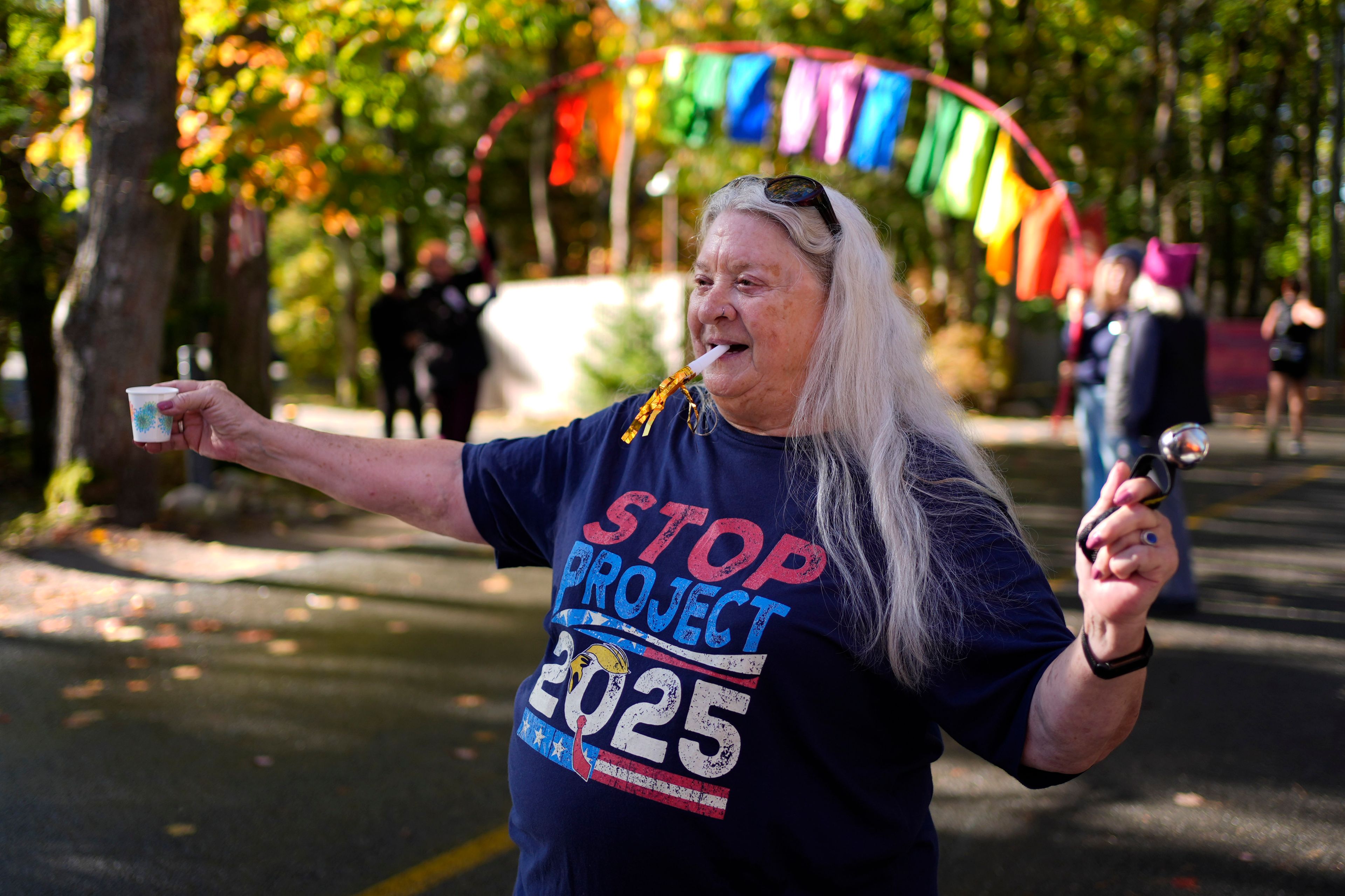 Carolyn Maches holds water for runner during a protest in front of the home of Leonard Leo during the Mount Desert Island Marathon, Sunday, Oct. 20, 2024, in Northeast Harbor, Maine. (AP Photo/Robert F. Bukaty)