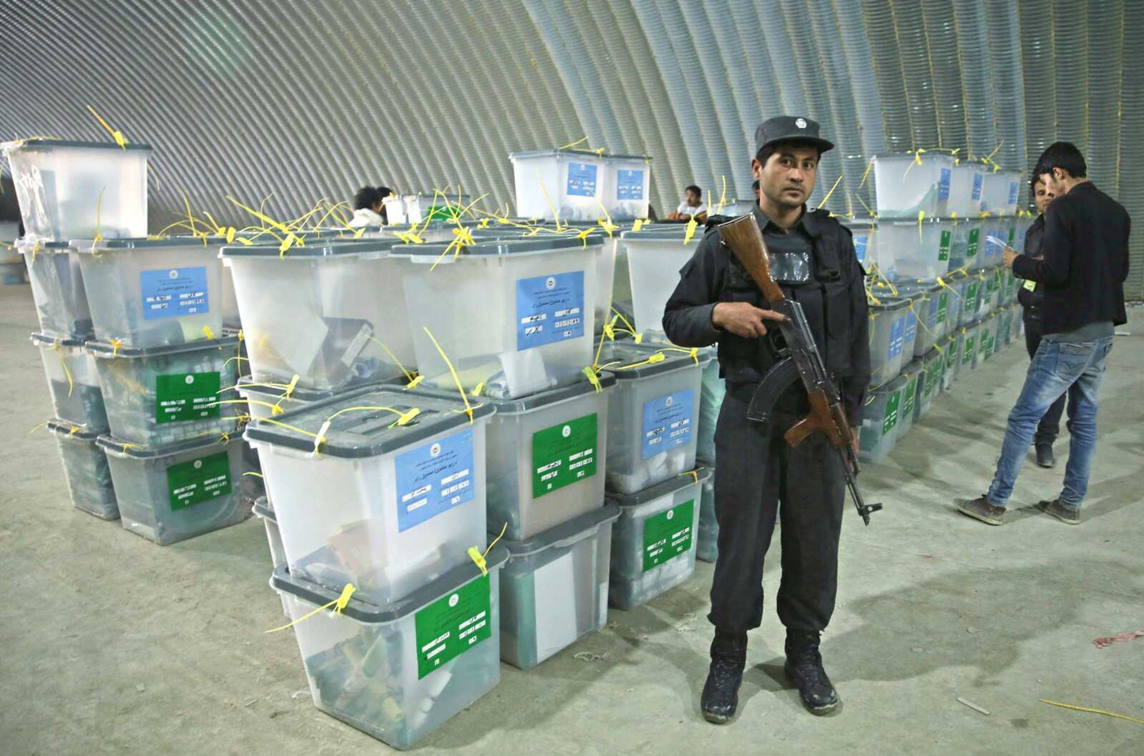 An Afghan police officer stands guard Sunday as Afghan election workers, right, note serial numbers of ballot boxes at a warehouse of the Independent Elections Commission warehouse in Kabul, Afghanistan. (Massoud Hossaini ~ Associated Press)