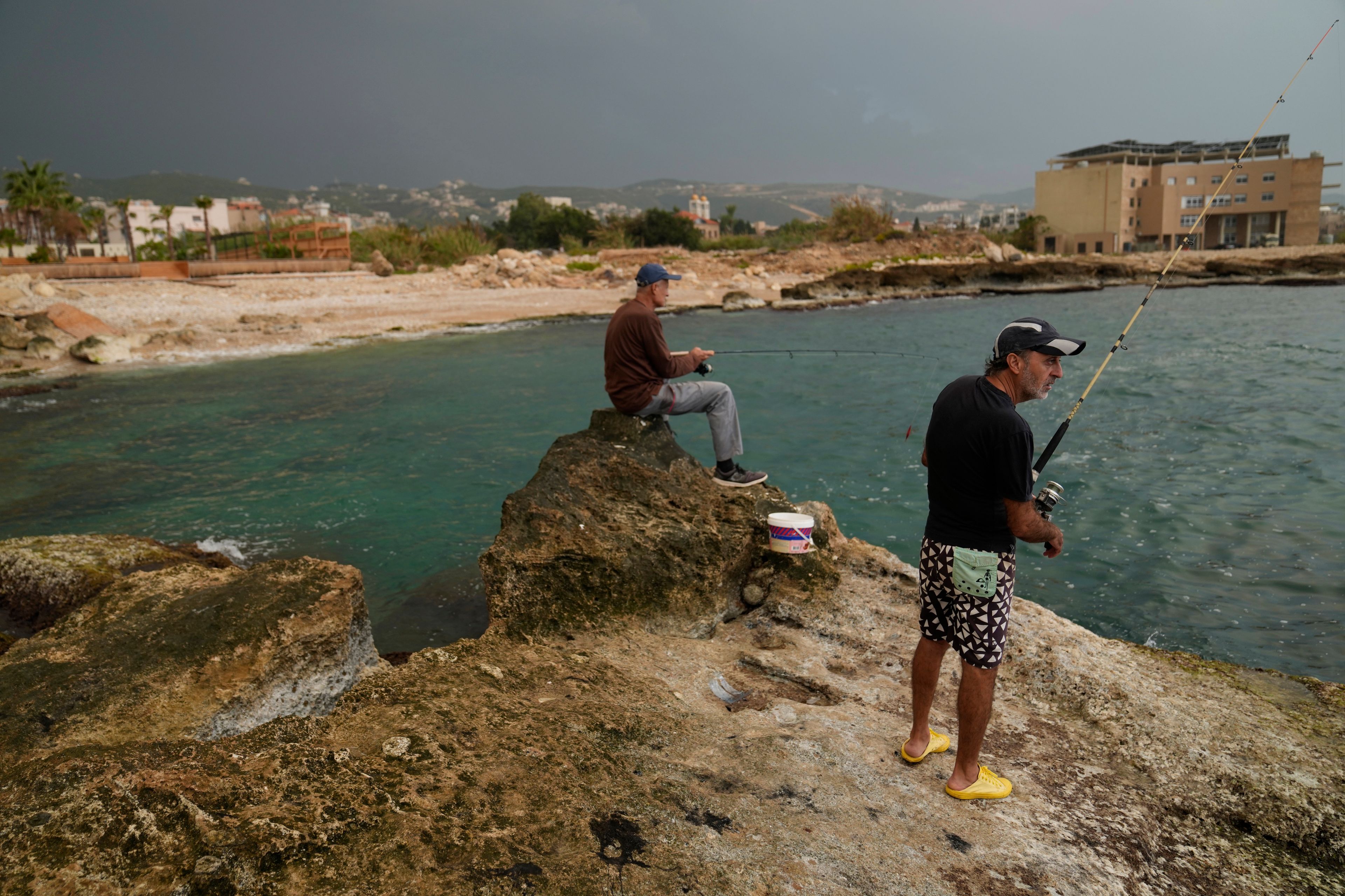 Lebanese fishermen cast their fishing rods at a beach in Batroun, northern Lebanon, Saturday, Nov. 2, 2024, where Lebanese officials say a ship captain was taken away by a group of armed men who landed on a coast north of Beirut and they're investigating whether Israel was involved. (AP Photo/Hussein Malla)